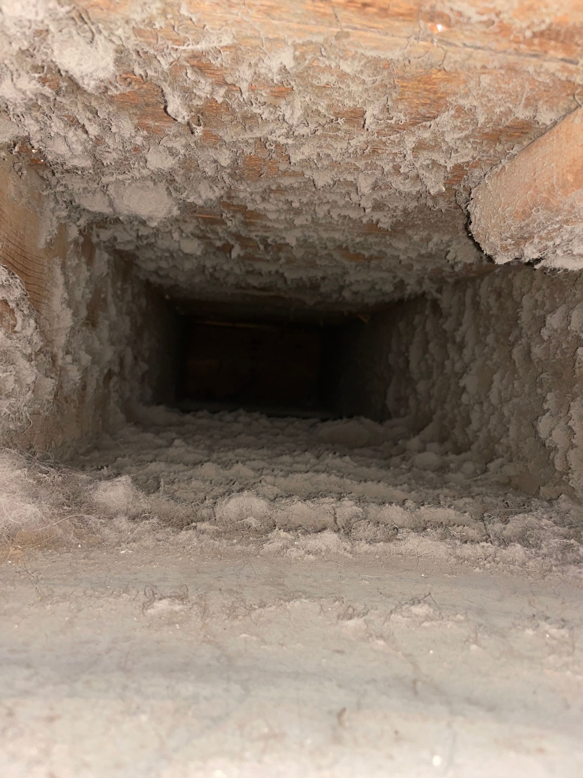 Narrow rocky tunnel leading into a dark cave, with rough stone walls and dusty floor.