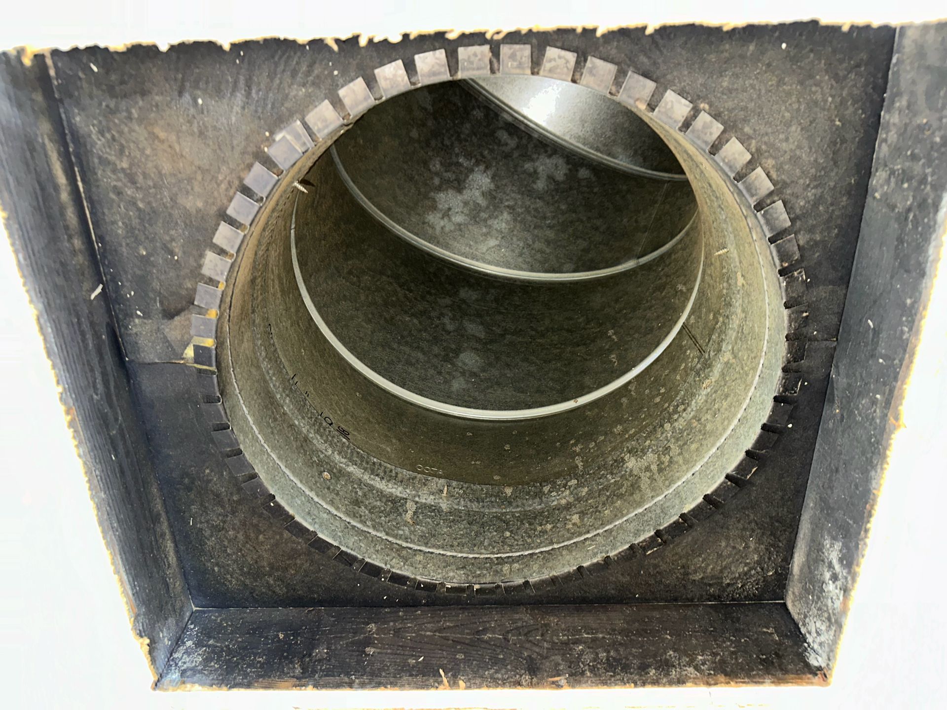 Close-up of a round metal ventilation duct inside a square opening, with dark insulation around it