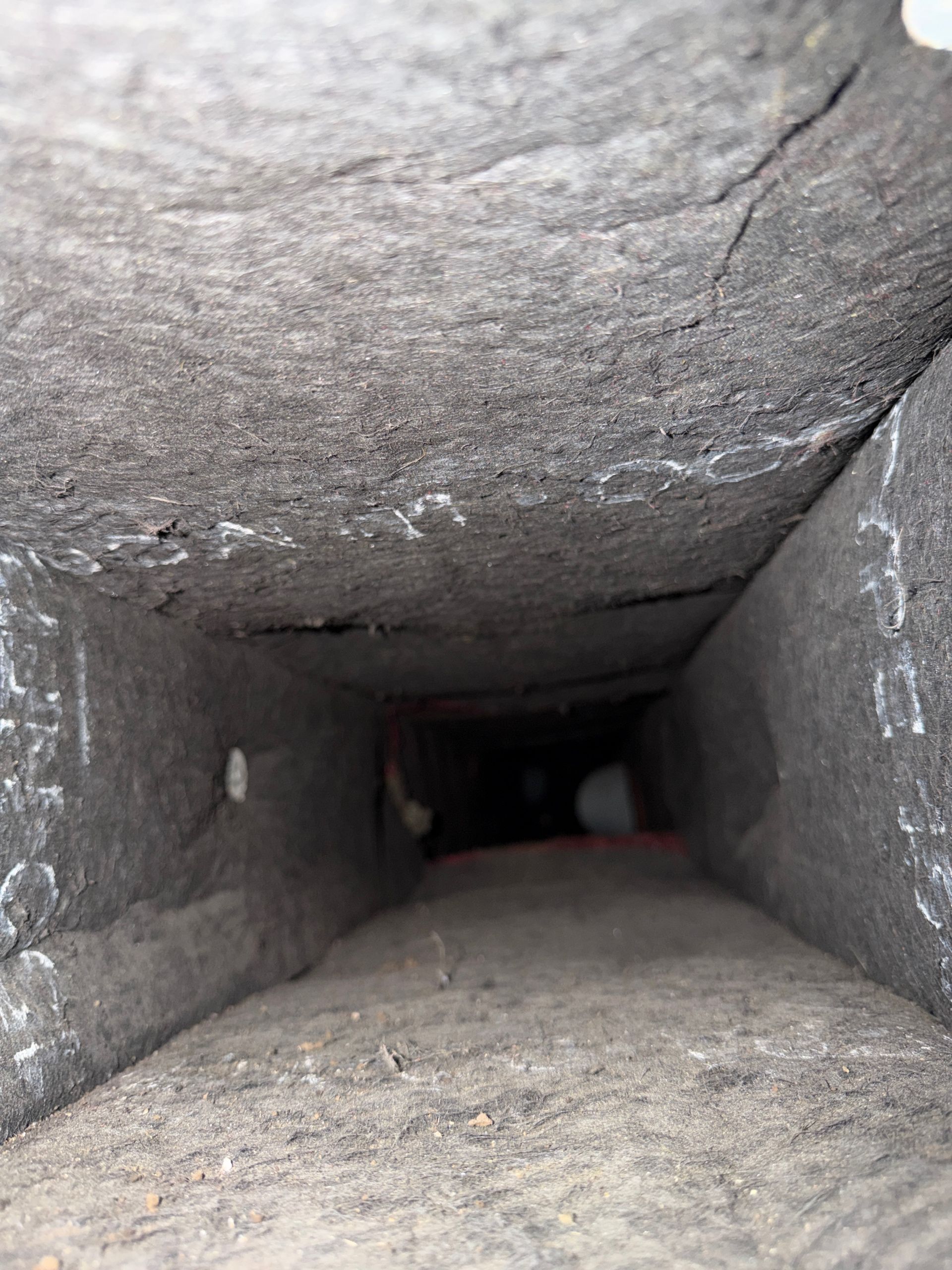 Narrow dark stone tunnel with rough walls and floor, leading into darkness