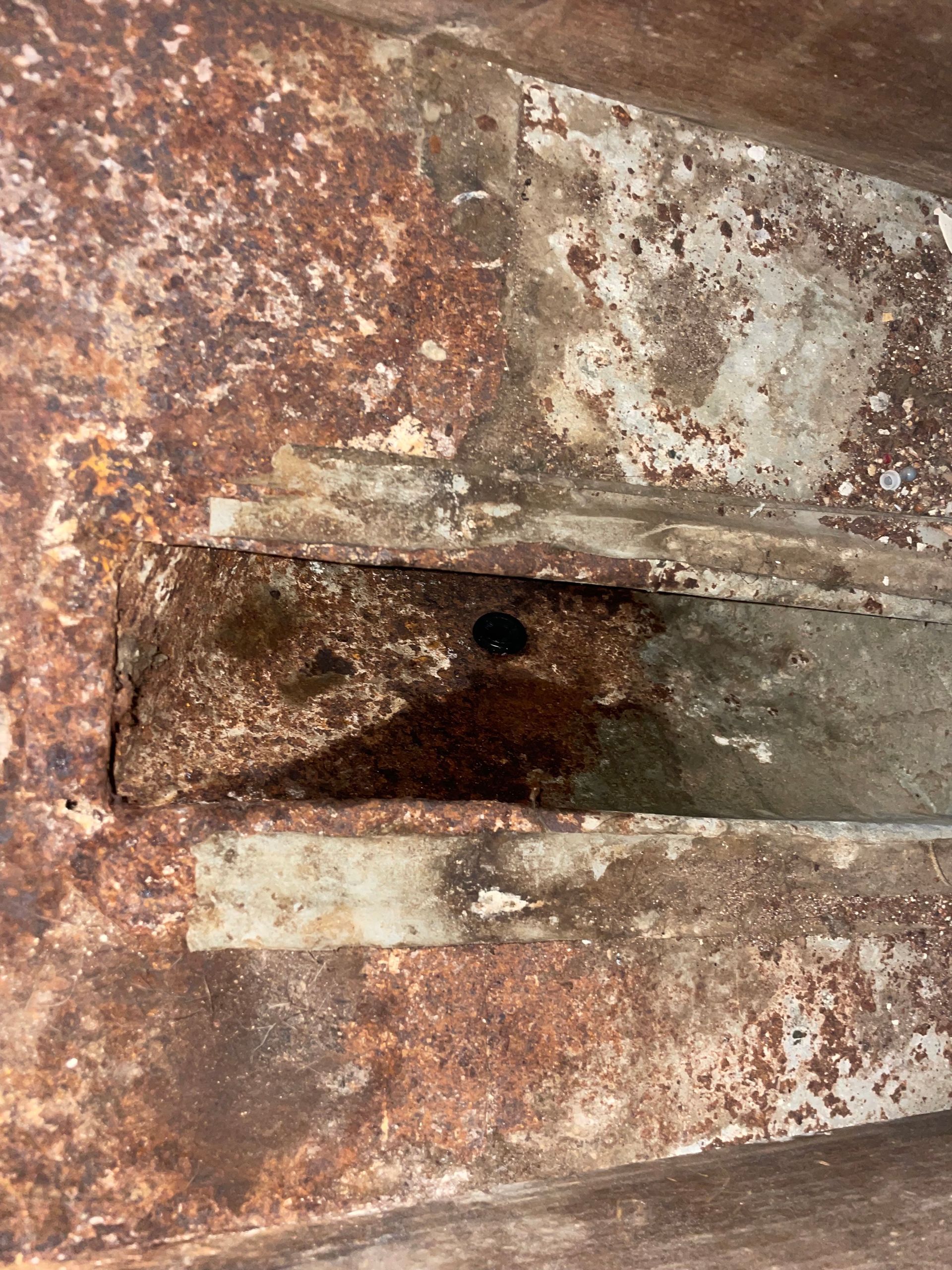 Rusty metal latch on a weathered surface, with a small hole and flaking paint.