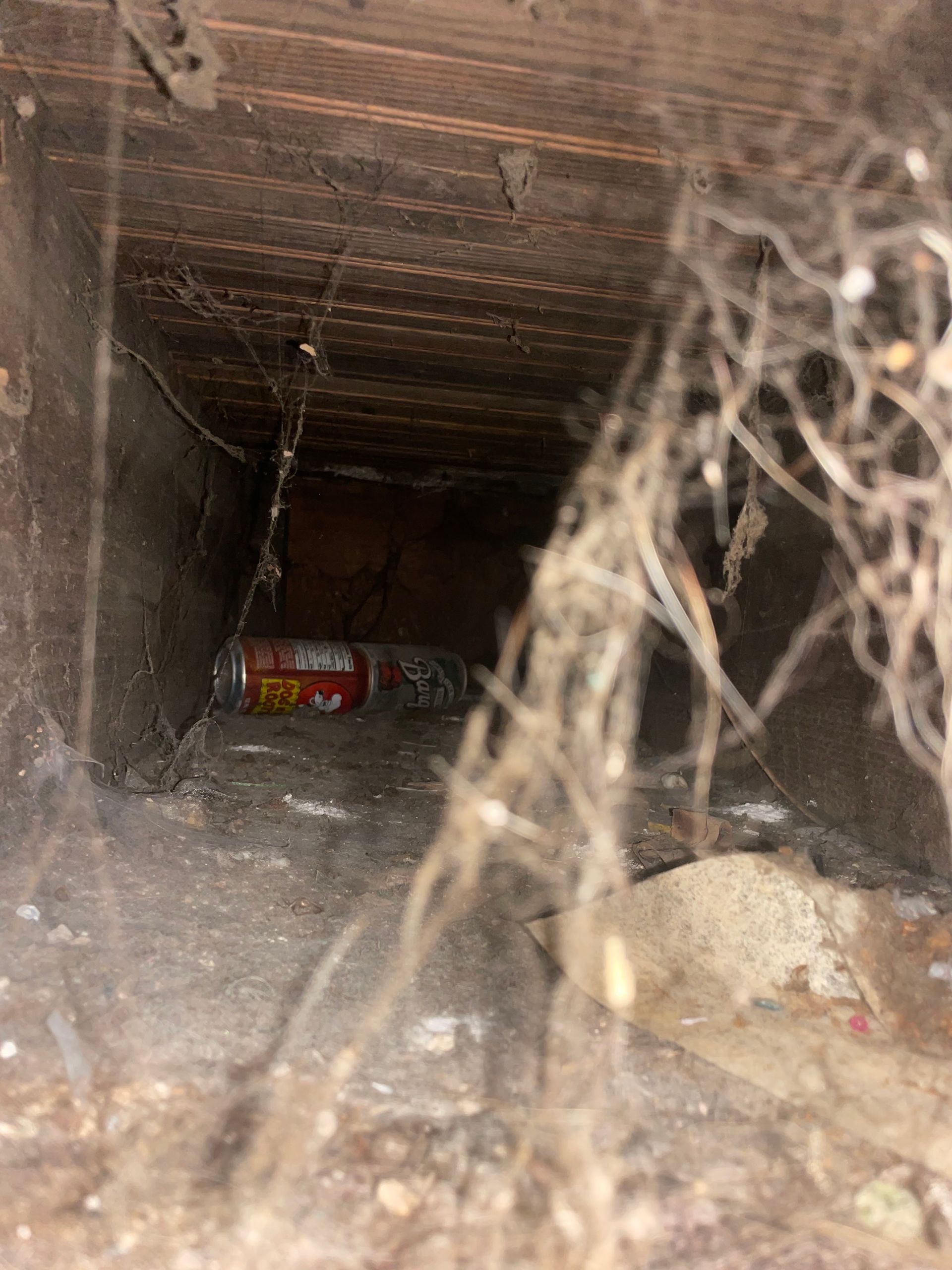 Inside a dusty duct or crawlspace with cobwebs and a red can lying on the floor.