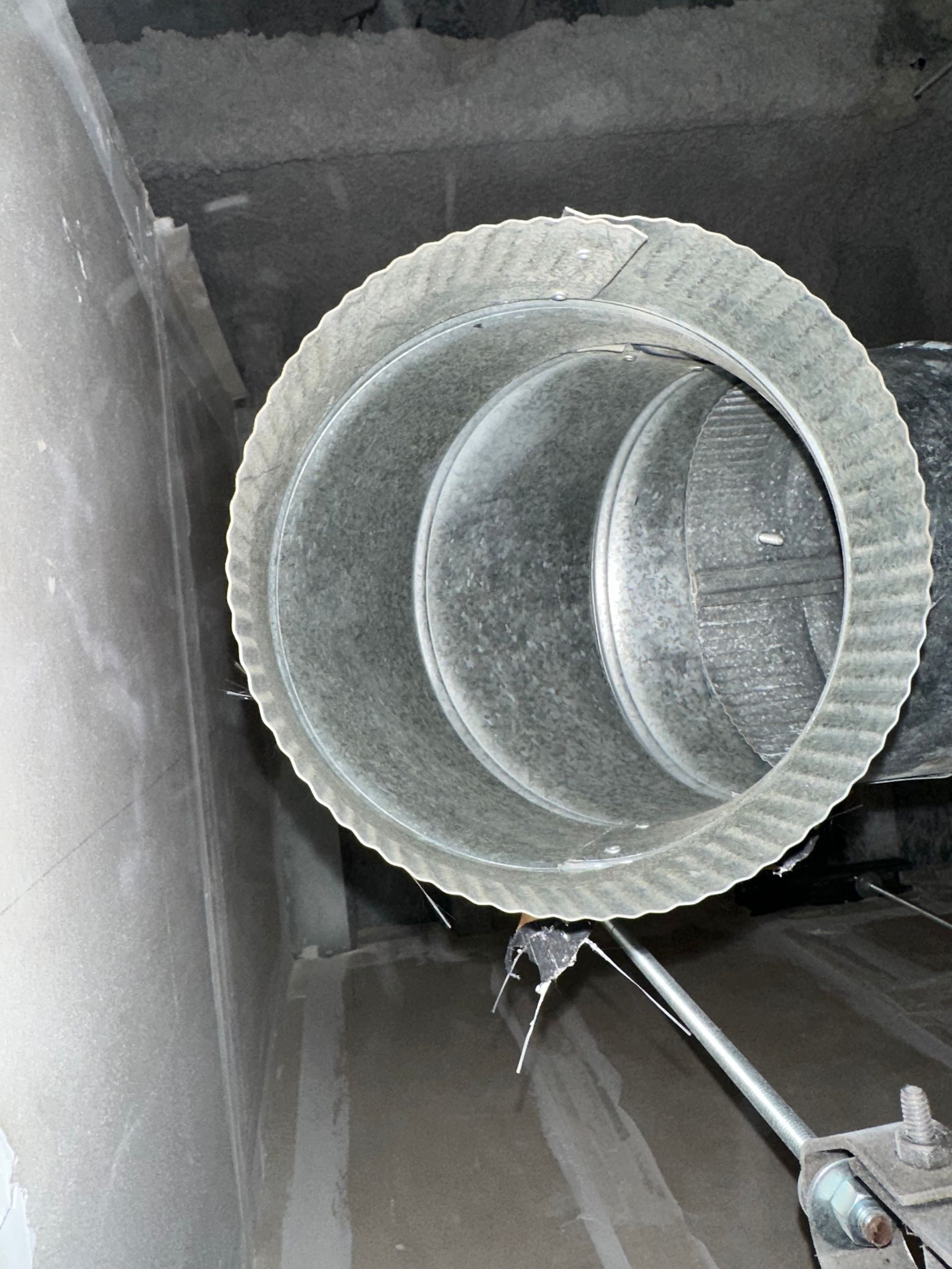 Close-up of a round, dusty ventilation duct with a metal rod inside a gray industrial space