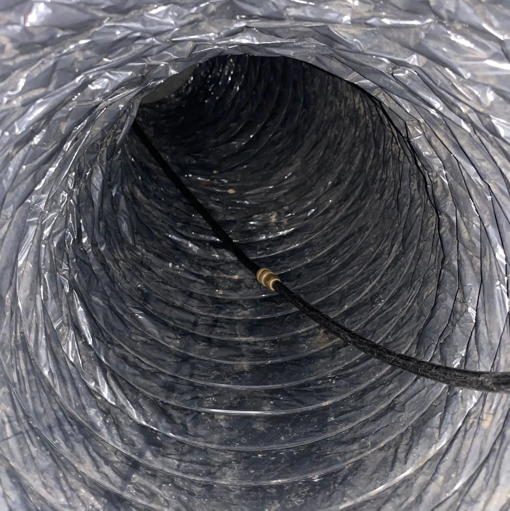 Inside a silver corrugated duct, a black cable runs through the center.