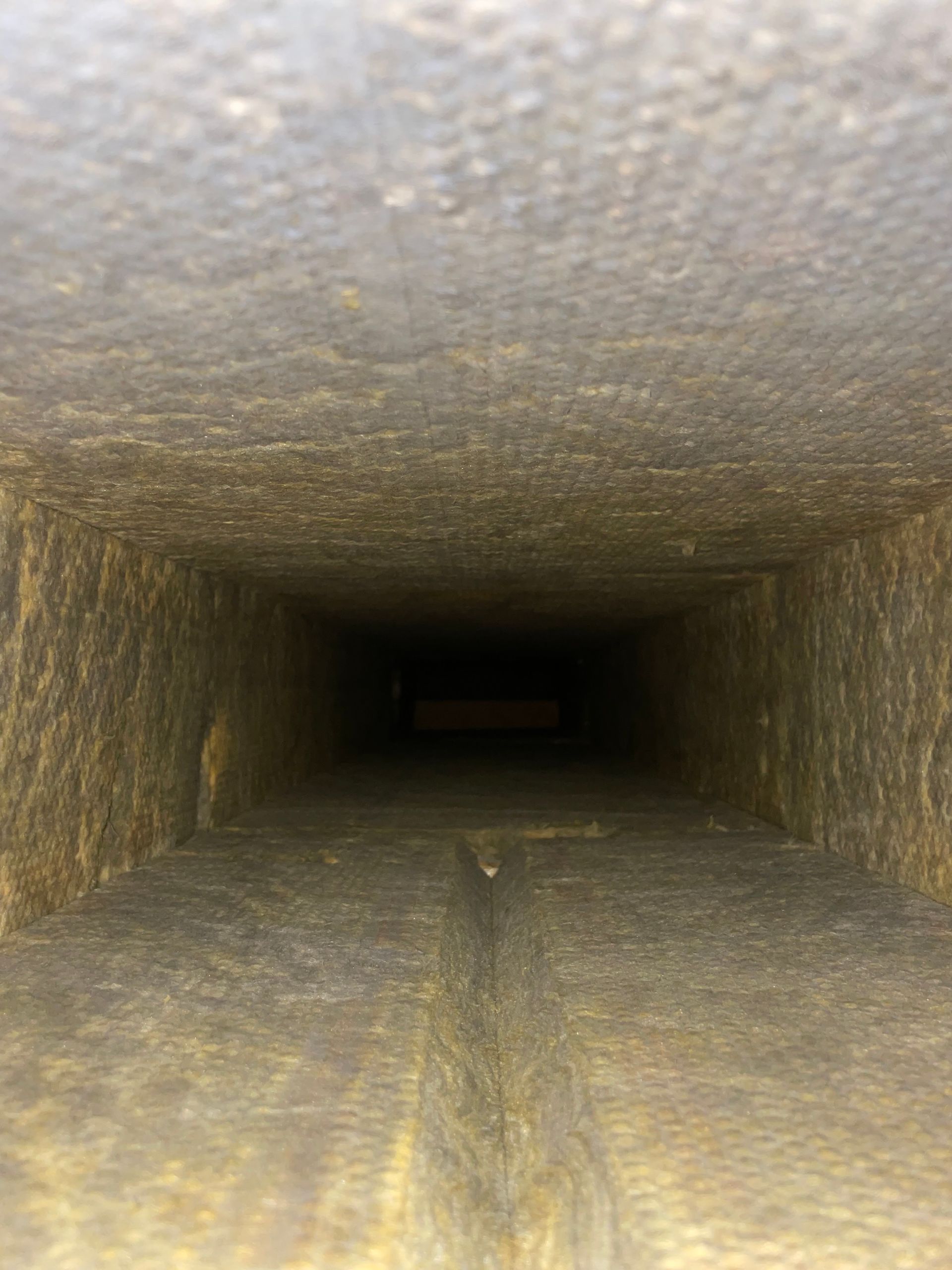 Rectangular duct interior with rough, textured walls fading into darkness