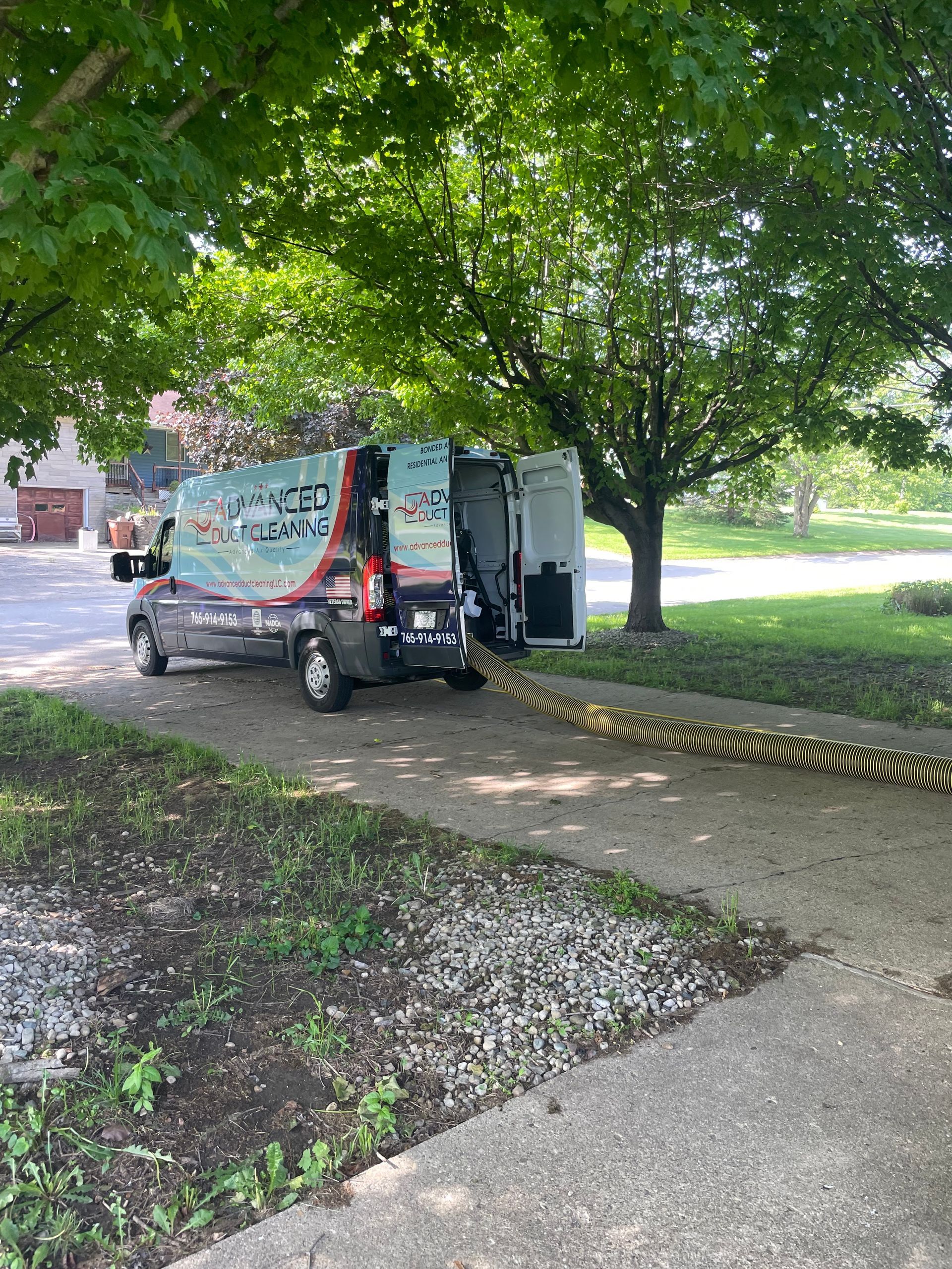 Trash truck parked on a leafy residential street beside a sidewalk and trees