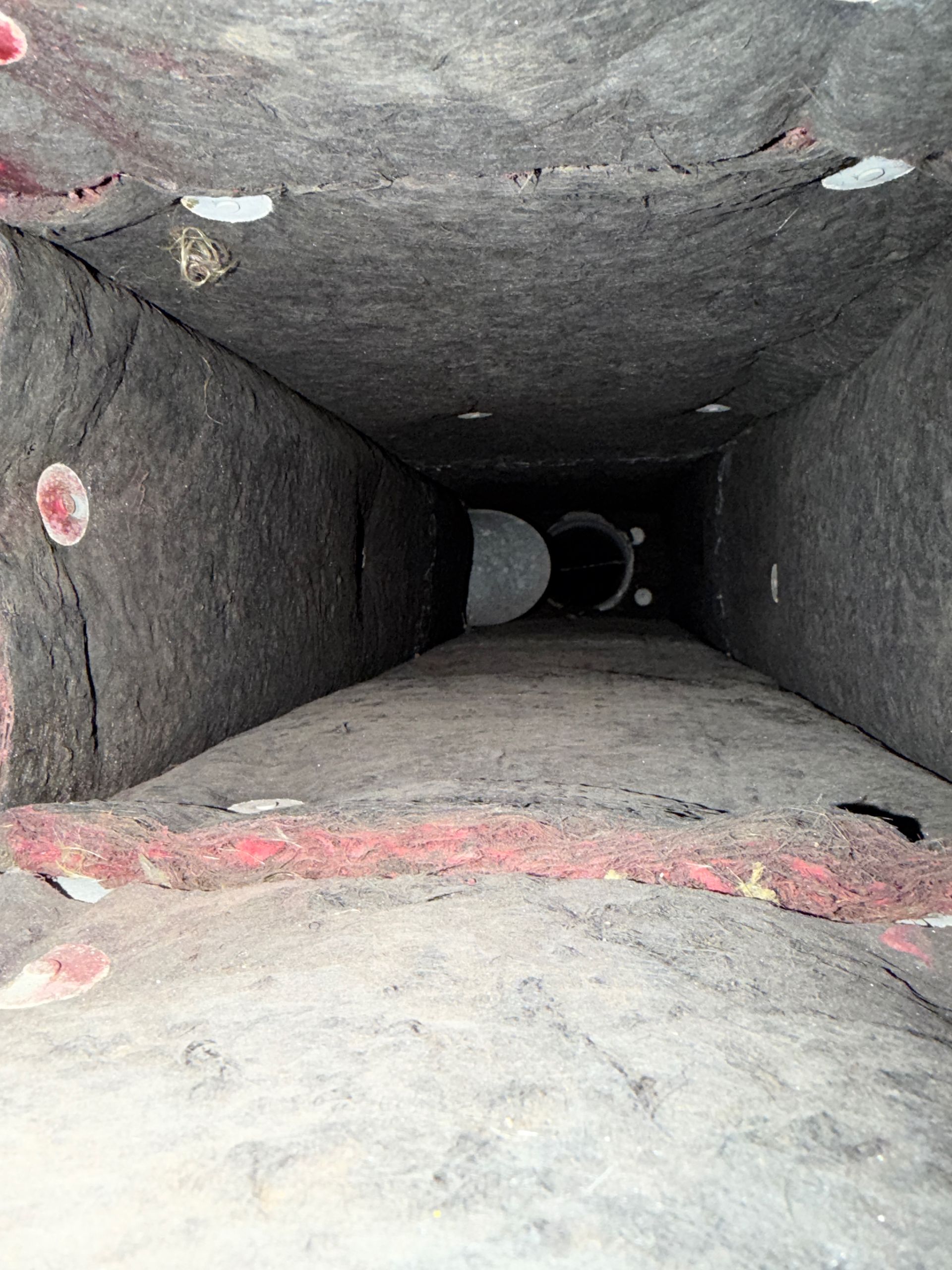Inside a dusty rectangular ventilation duct with rough gray walls and red patches at the edges.