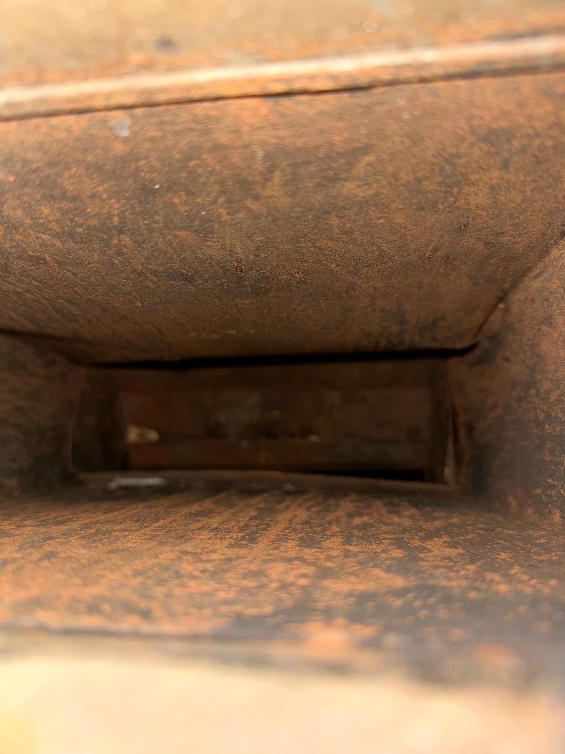 Rusty metal duct interior with a narrow rectangular opening in the center