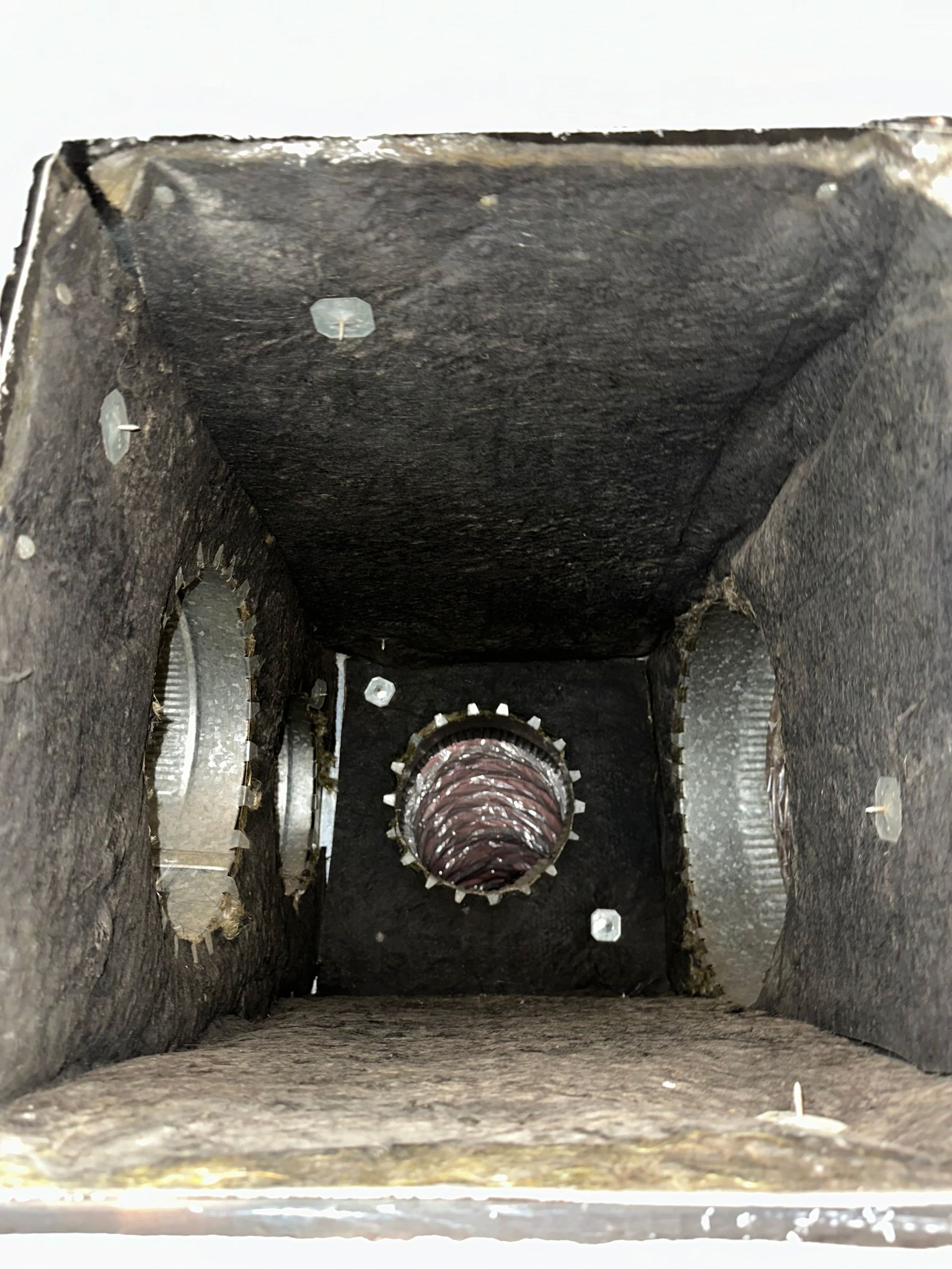 Inside of a dusty metal duct with a round fan or vent at the far end.