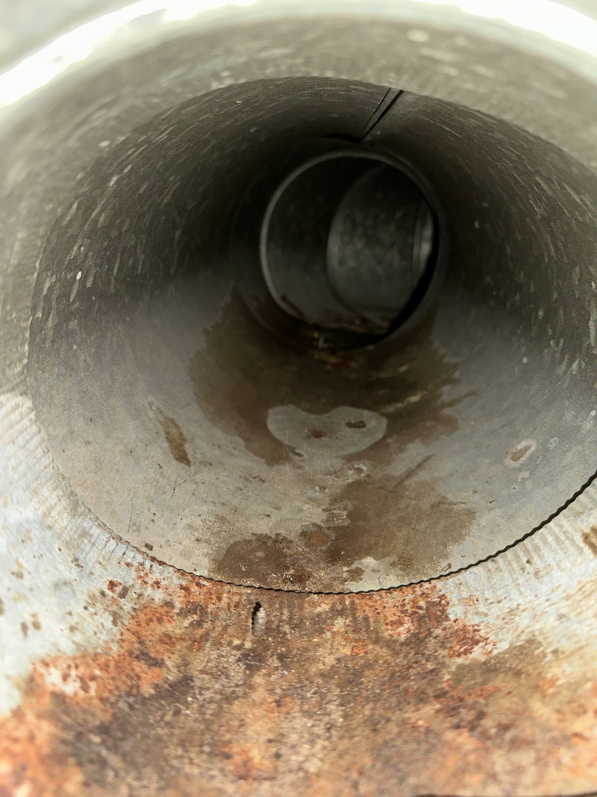Inside a metal pipe with rust stains and a small puddle at the bottom