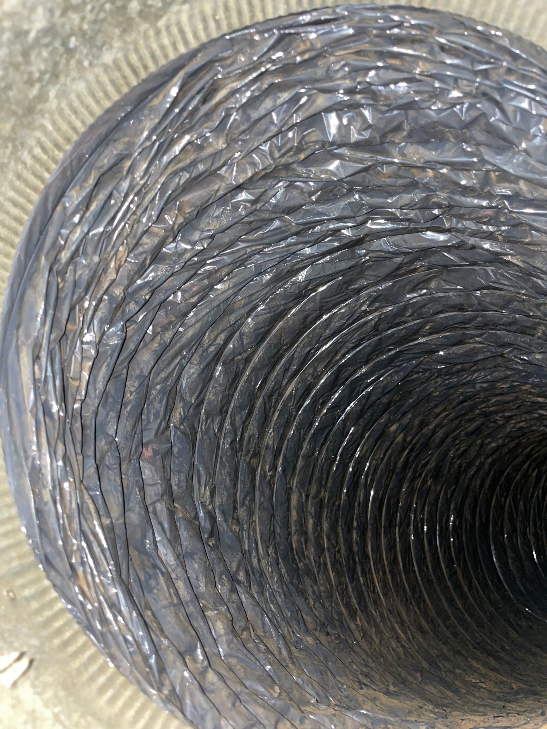 Looking down inside a corrugated metal duct or pipe with a dark circular tunnel opening