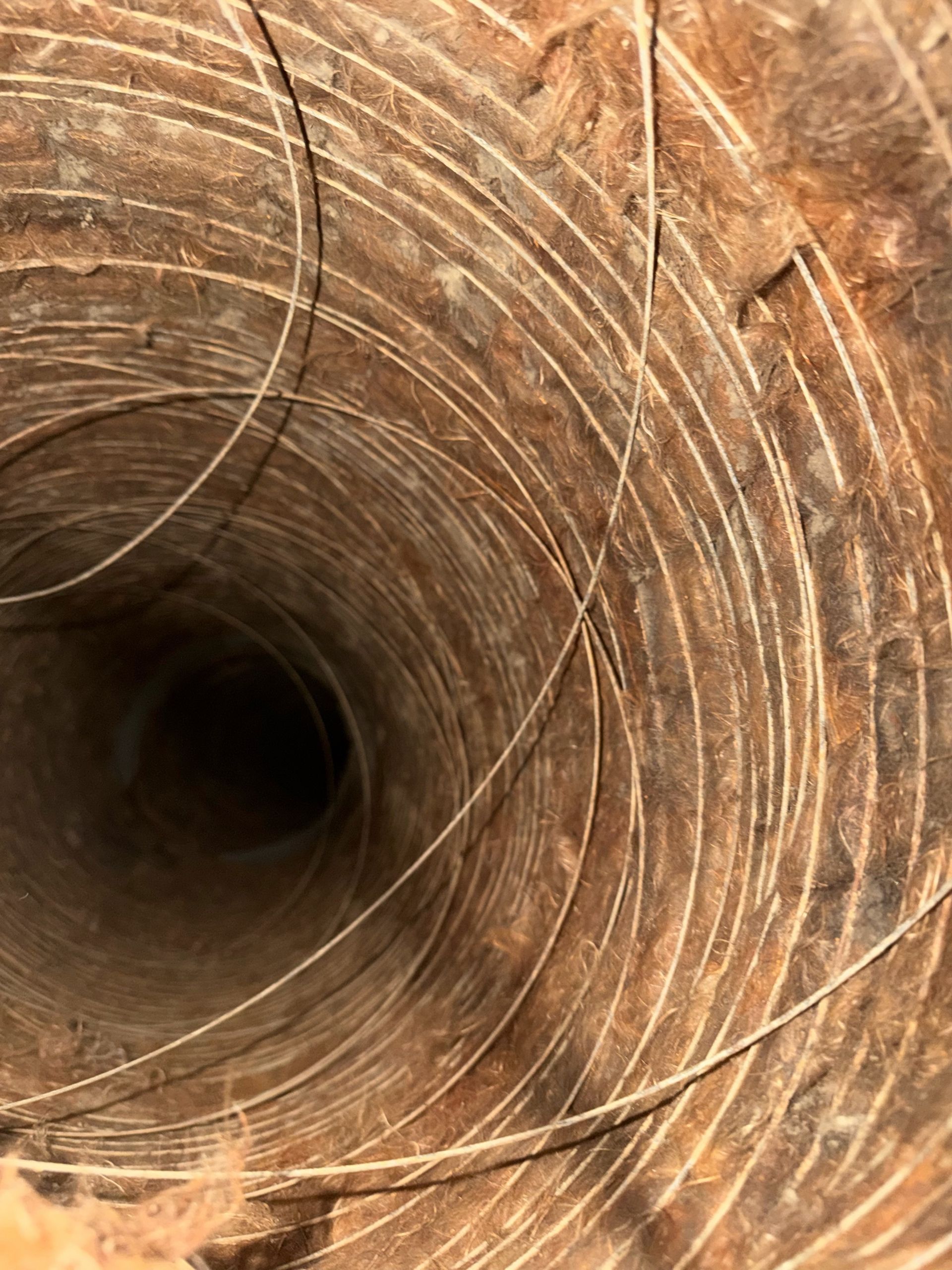Inside view of a rusted metal pipe or tunnel with concentric circular ridges and a dark opening