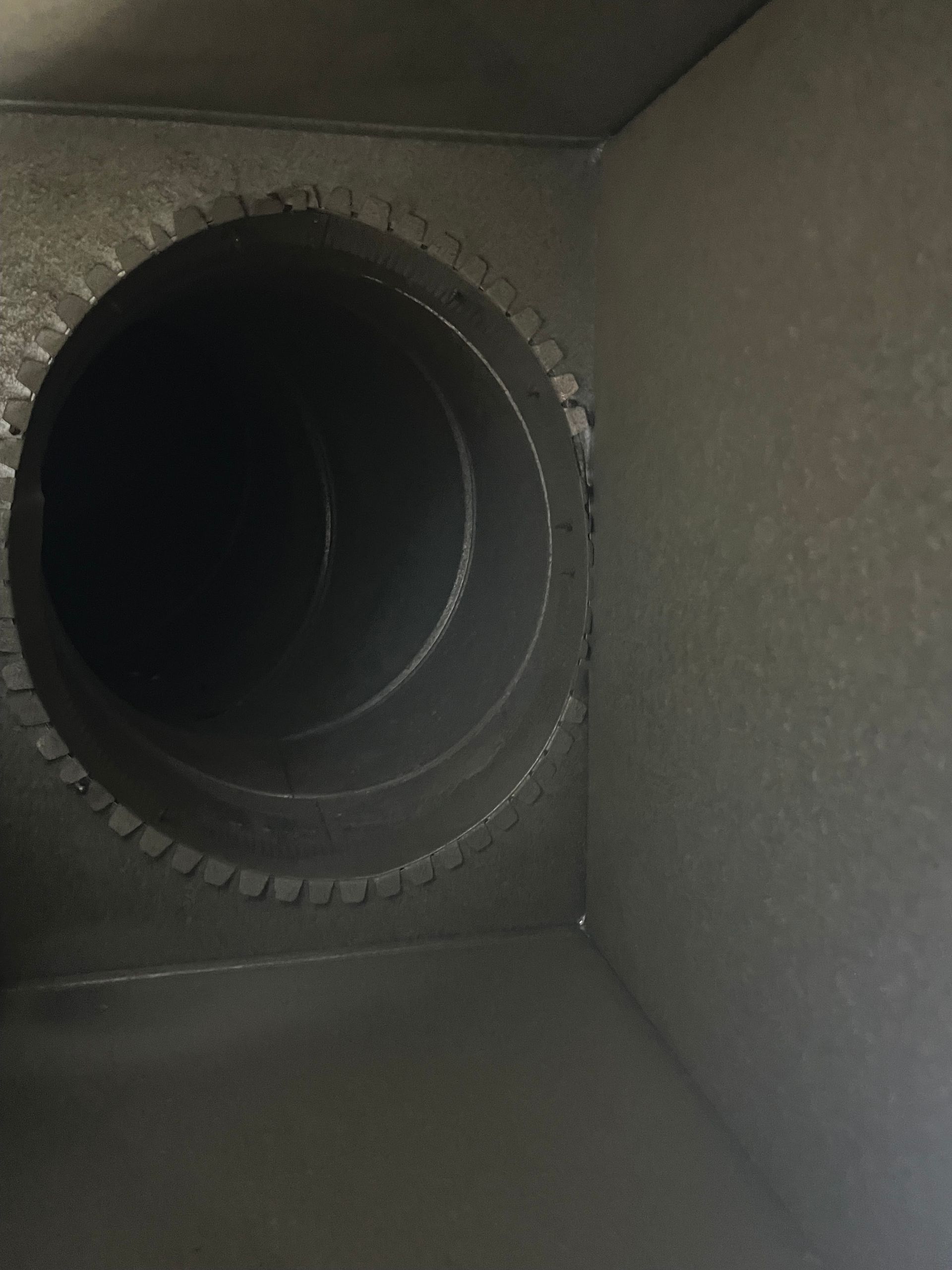 Inside view of a dark metal ventilation duct with a circular opening.