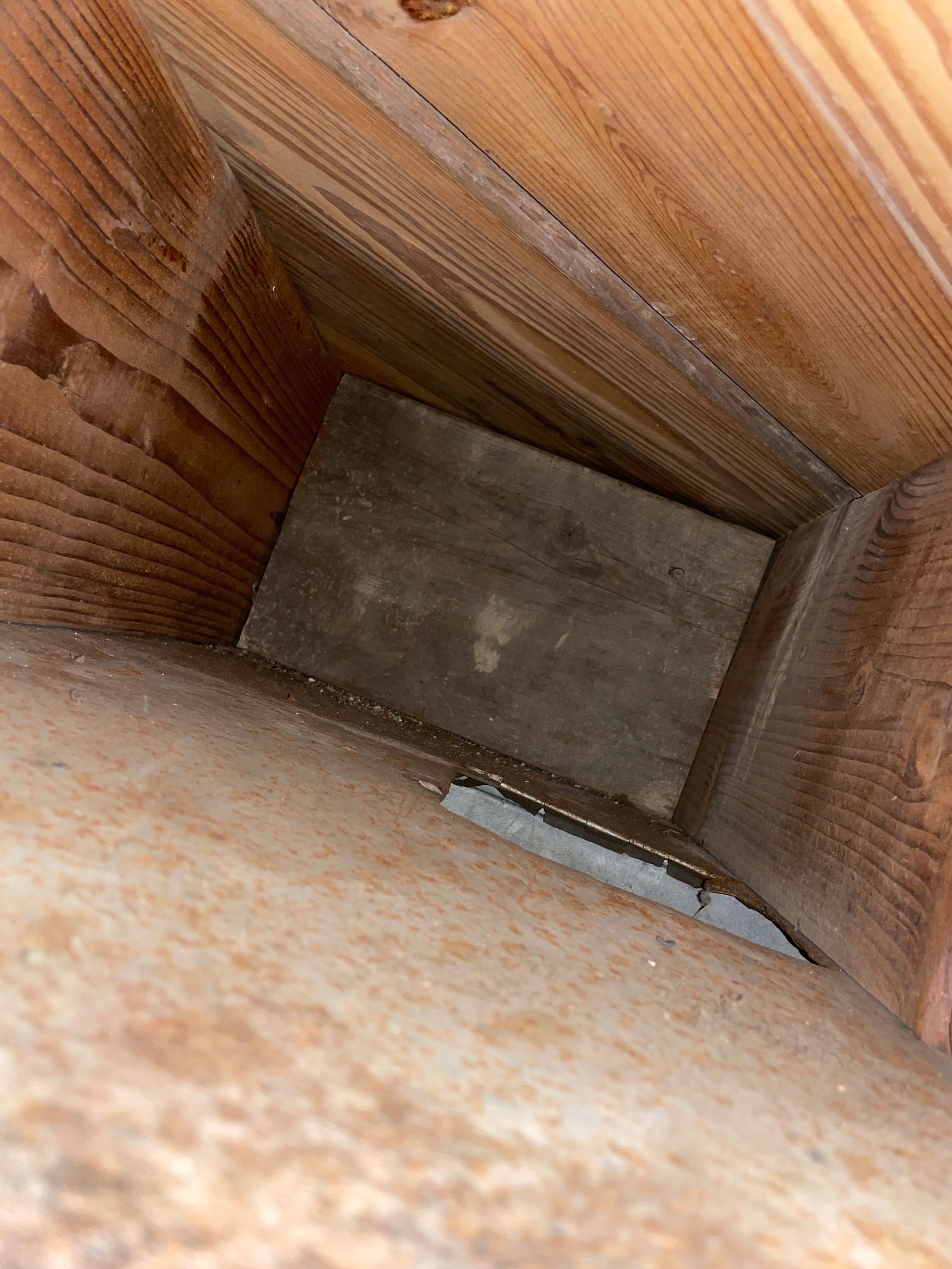 Looking down into a wooden box or narrow shaft with a gray bottom and a small white object inside
