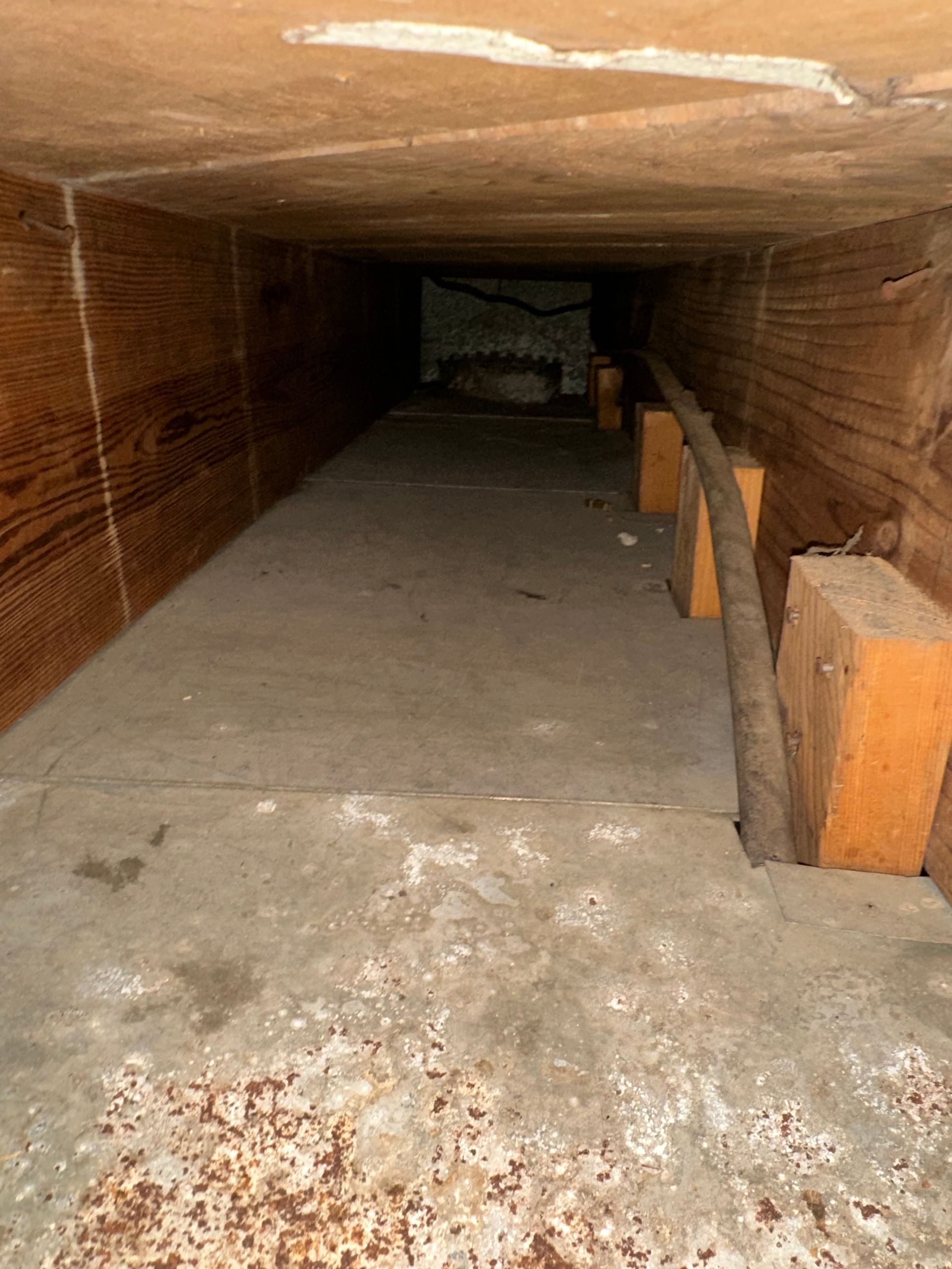 Narrow crawl space with a concrete floor, wooden supports, and low brick ceiling.