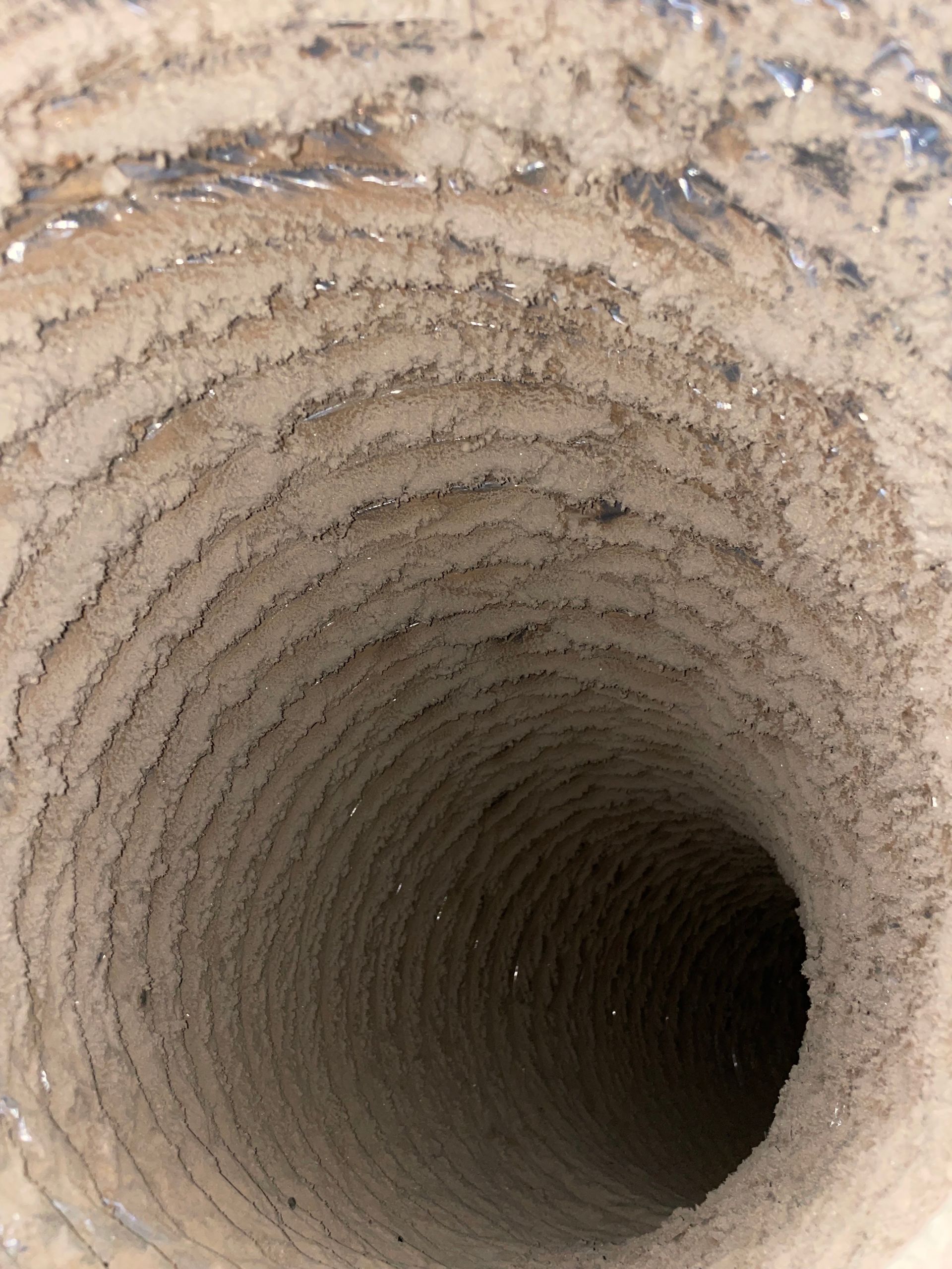 Inside a cylindrical clay or concrete well, looking down into a dark, spiraling shaft