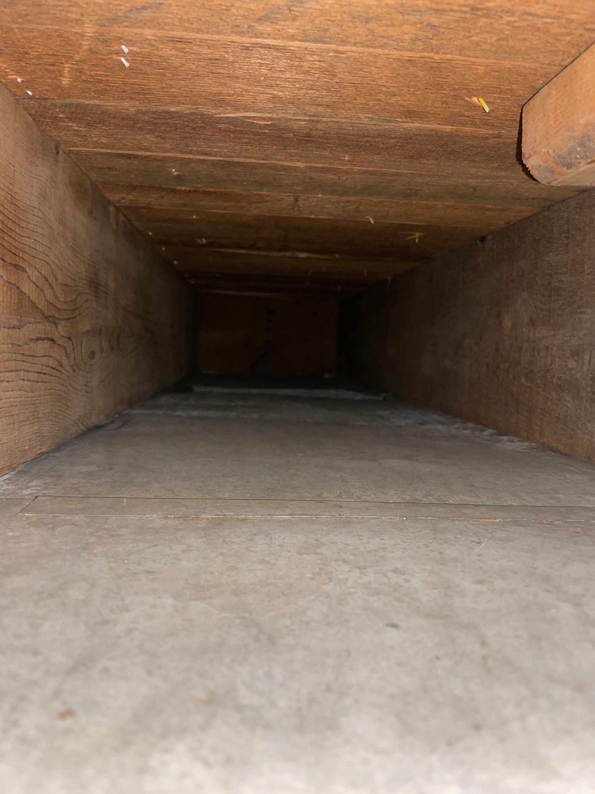 Inside a narrow wooden tunnel or duct, dark and empty.