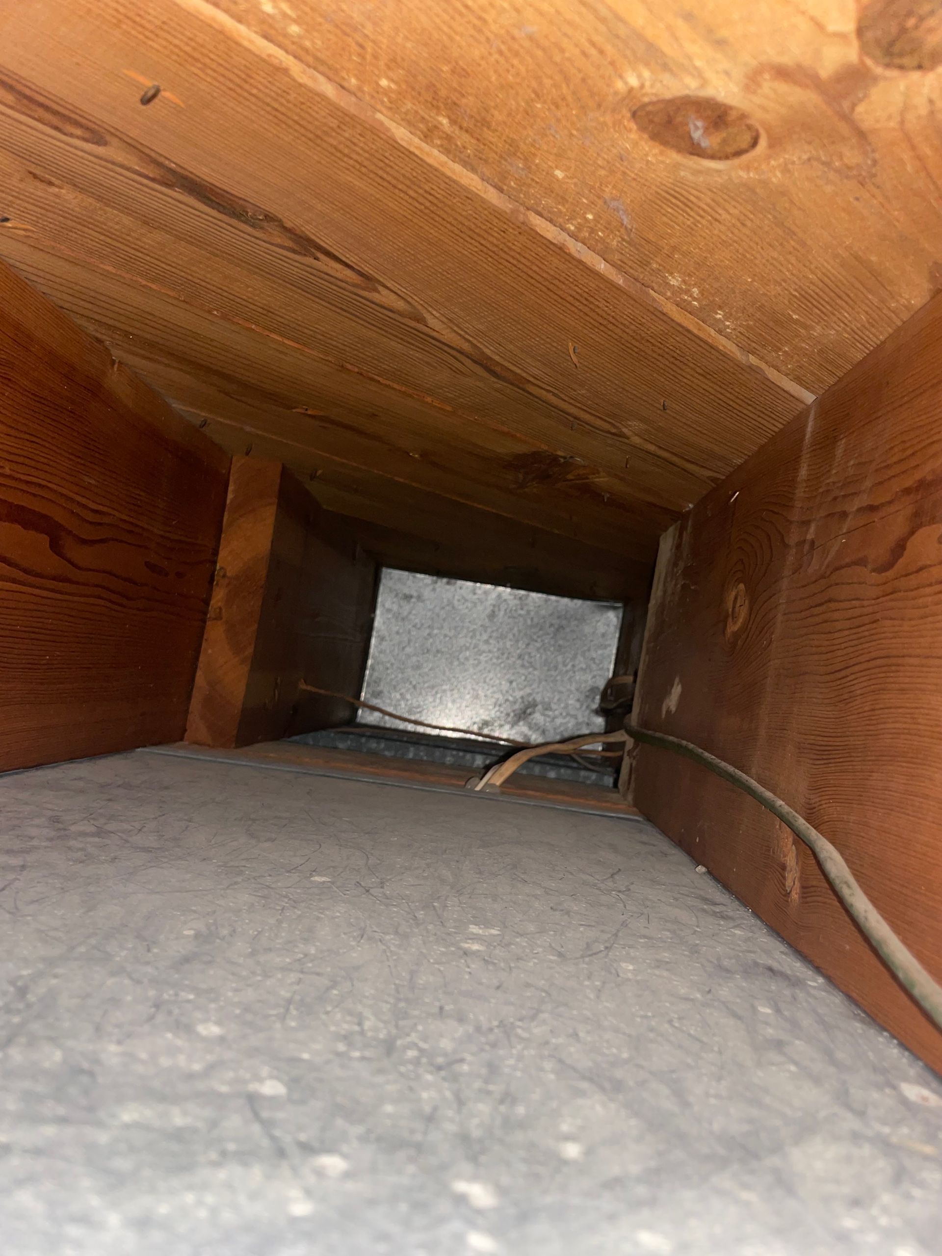 Inside a wooden crawlspace, with insulation and wiring along the floor and walls.