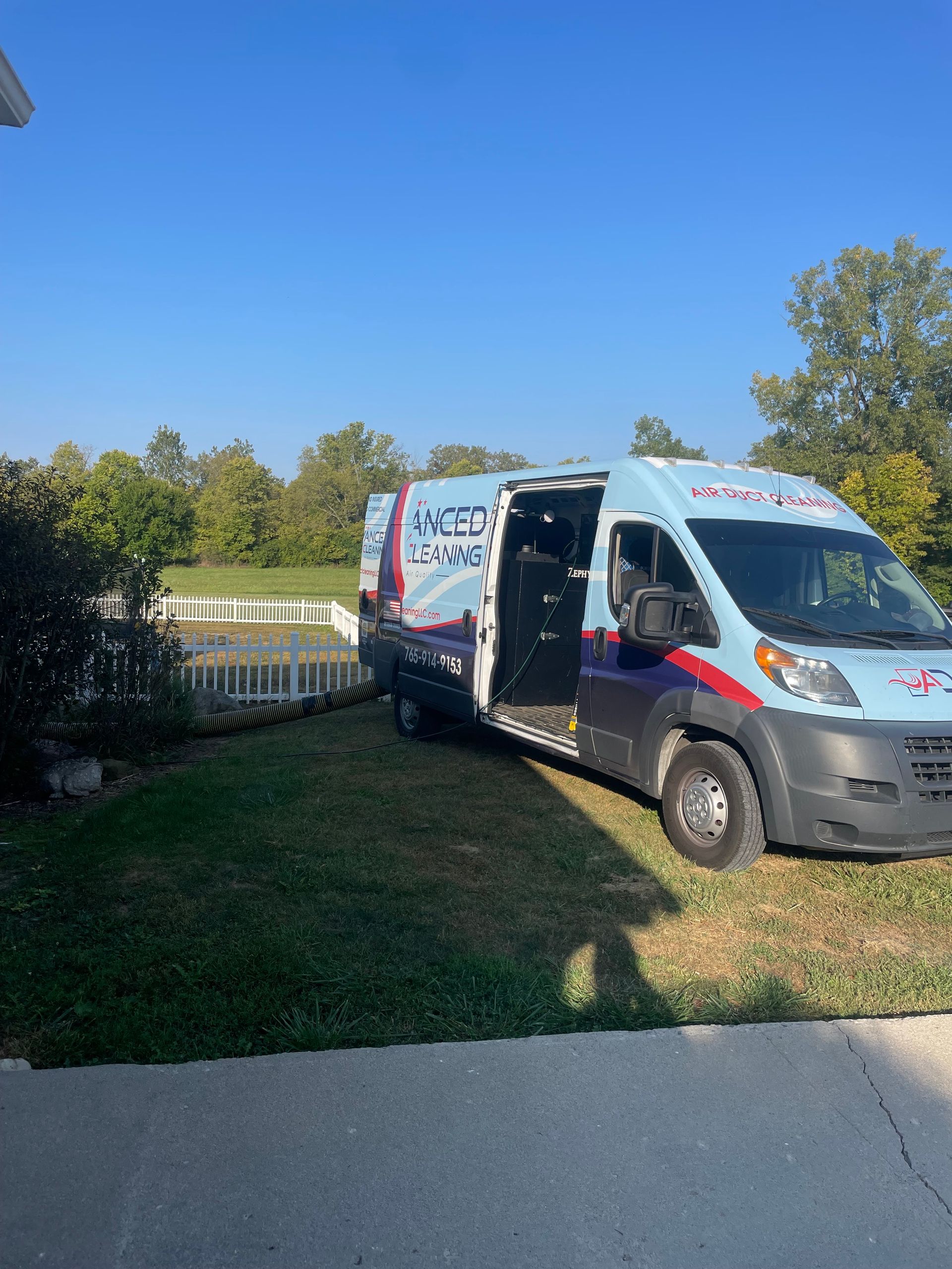 White service van parked on a grassy lawn beside a sidewalk on a sunny day