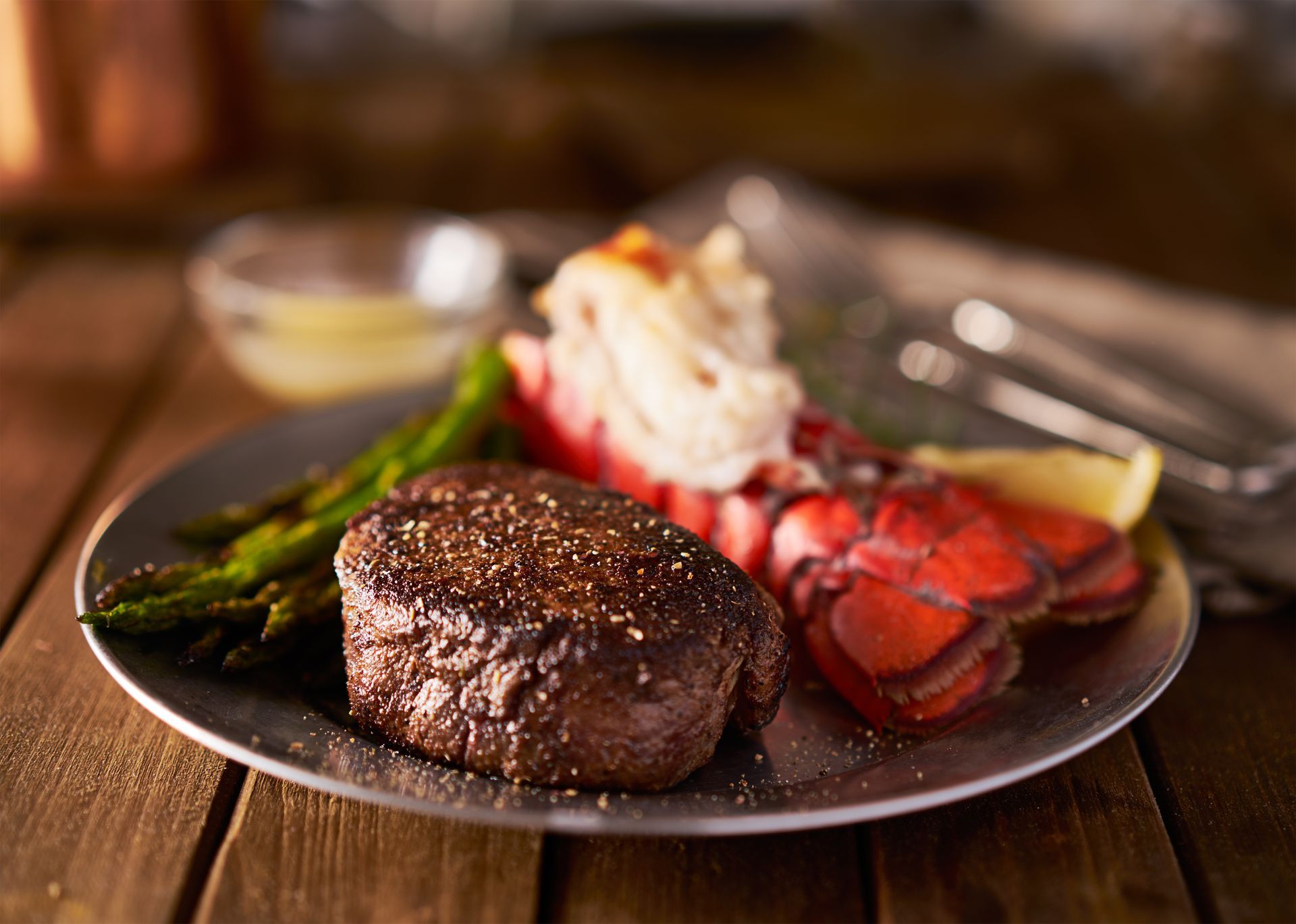 Steak dinner with lobster tail, asparagus, and mashed potatoes on a plate, on a wooden table