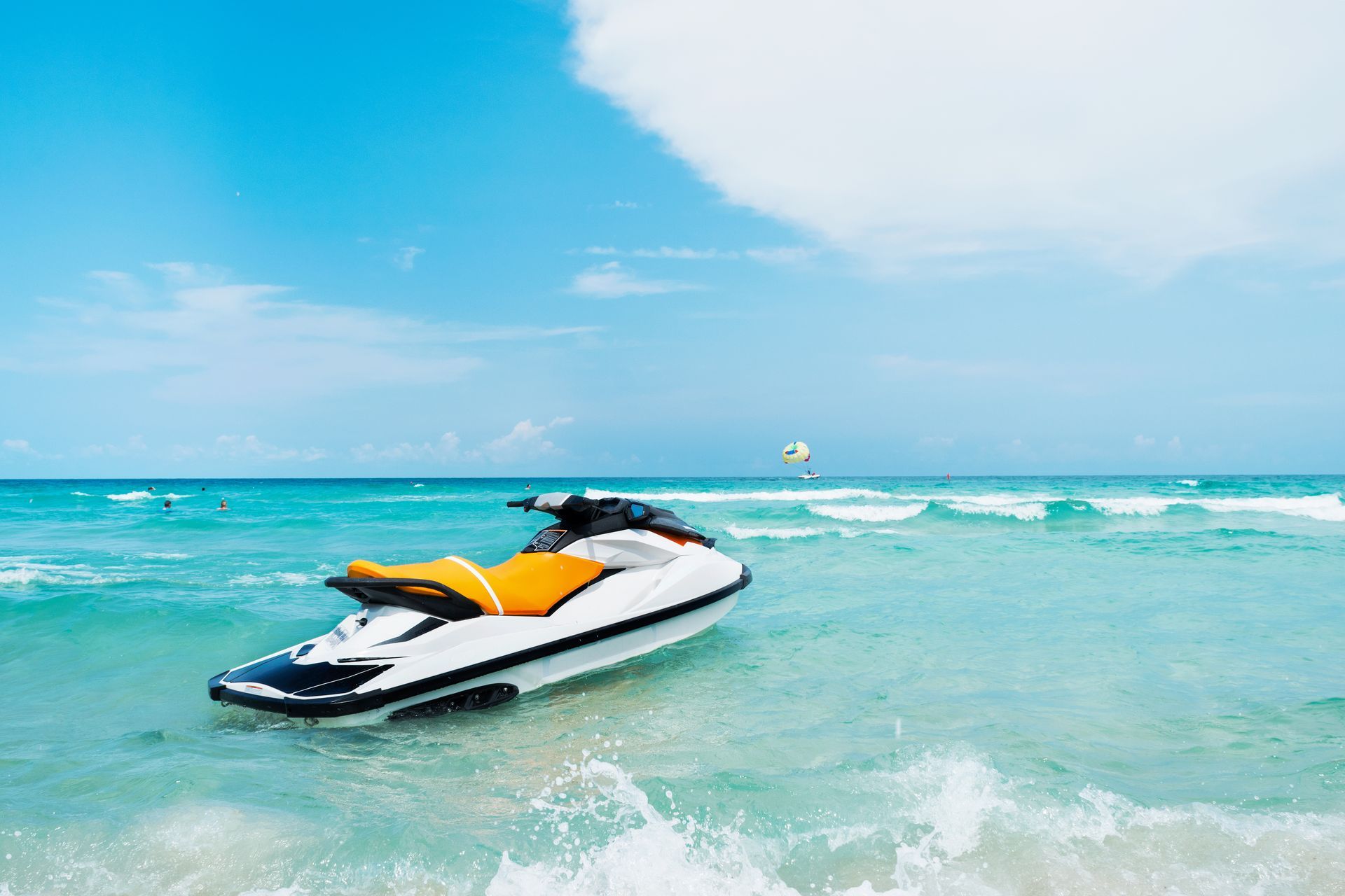 Jet ski with orange seat floating on turquoise water near a sandy beach under a blue sky