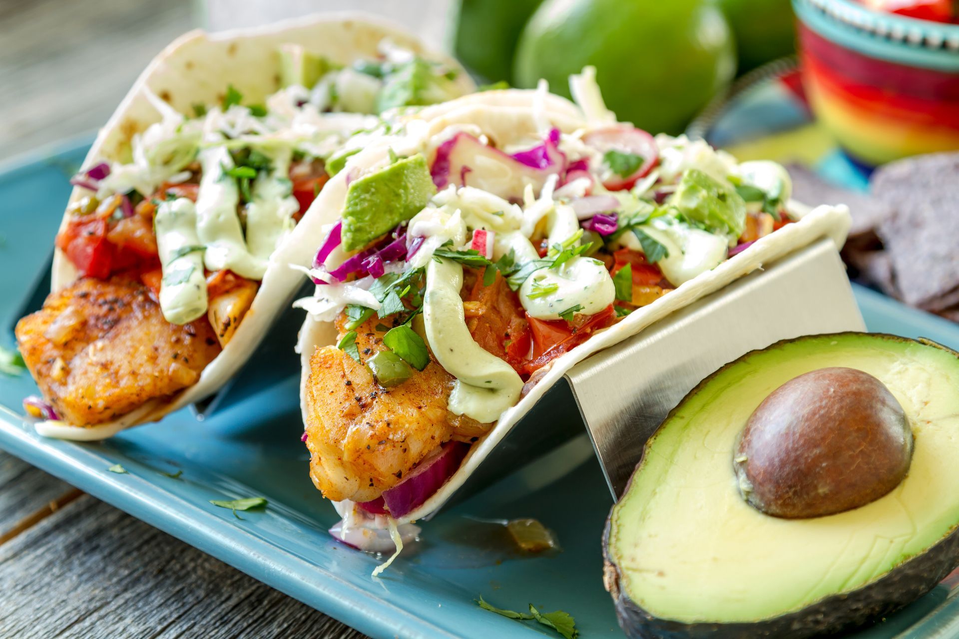 Two fish tacos on a blue plate with avocado slices and a lime in the background