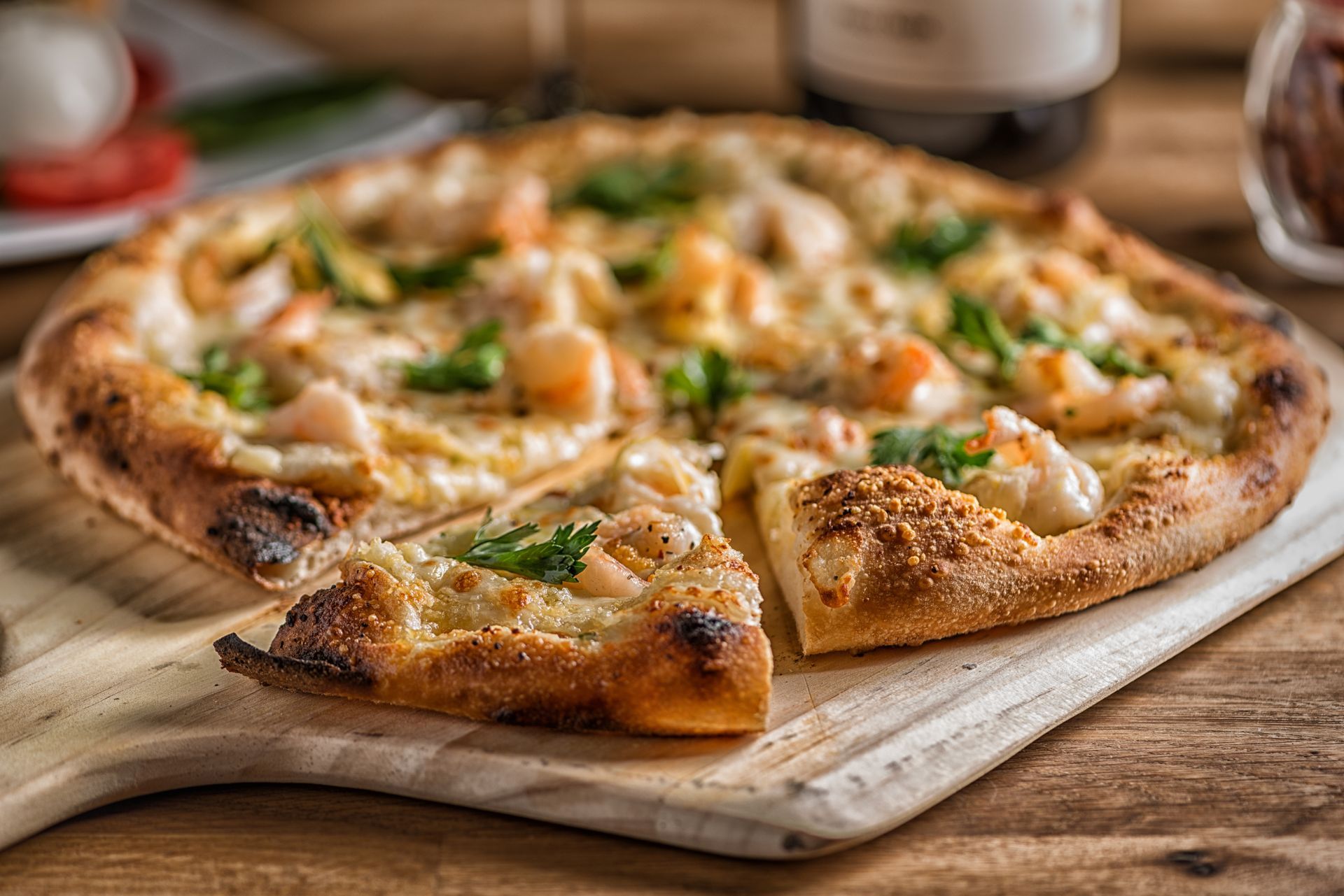 Fresh shrimp pizza on a wooden board, sliced and topped with herbs and cheese