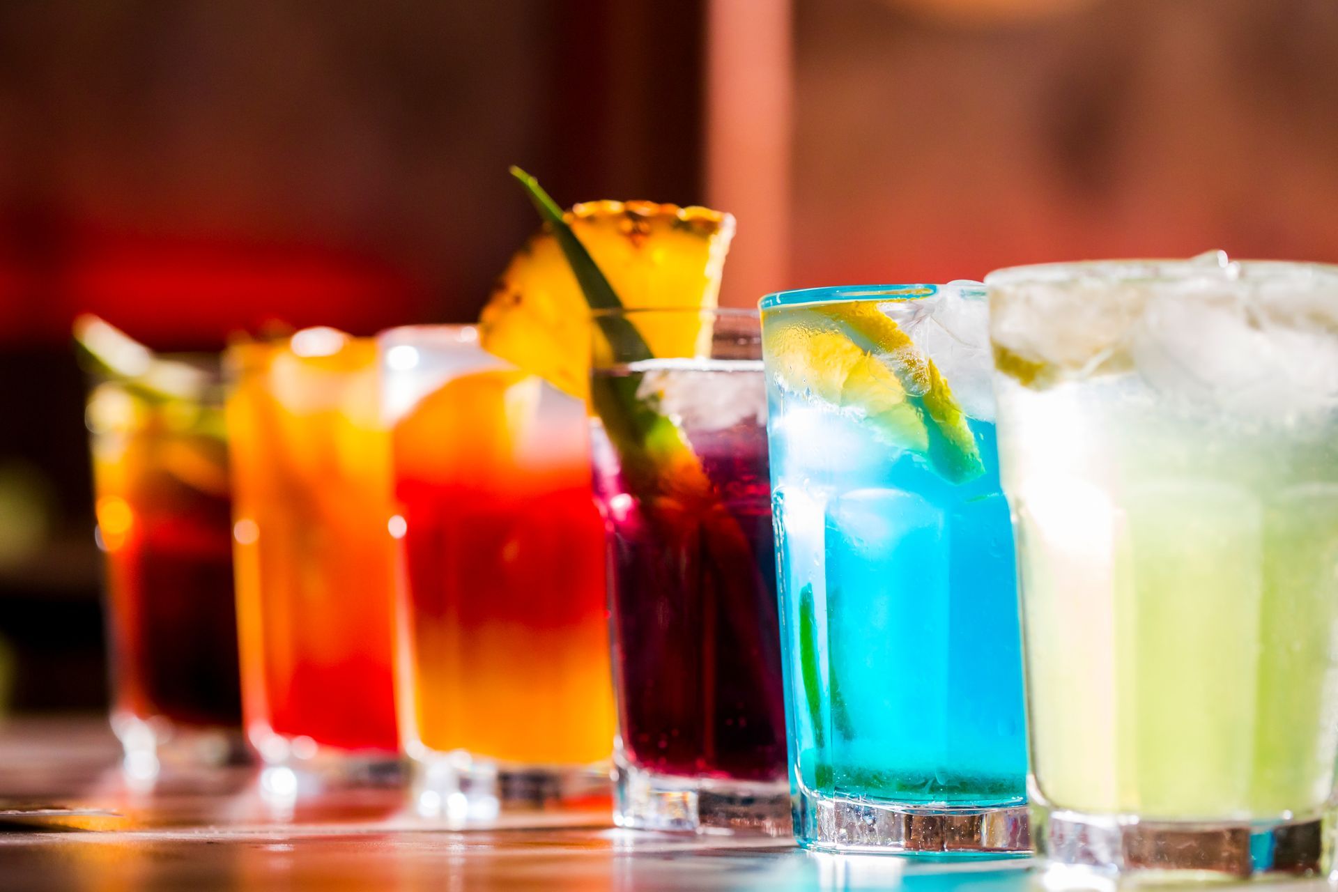 Colorful assorted cocktails in tall glasses on a bar counter, with ice and citrus garnishes