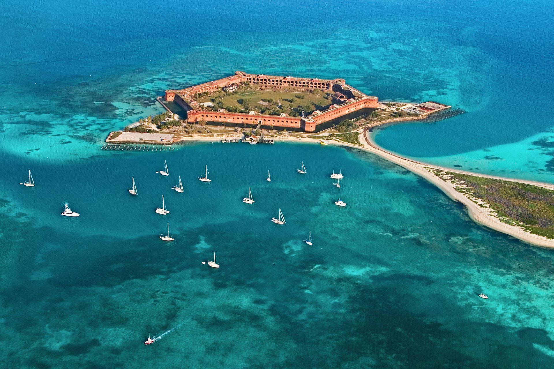 Aerial view of a small island fortress surrounded by turquoise water and several sailboats