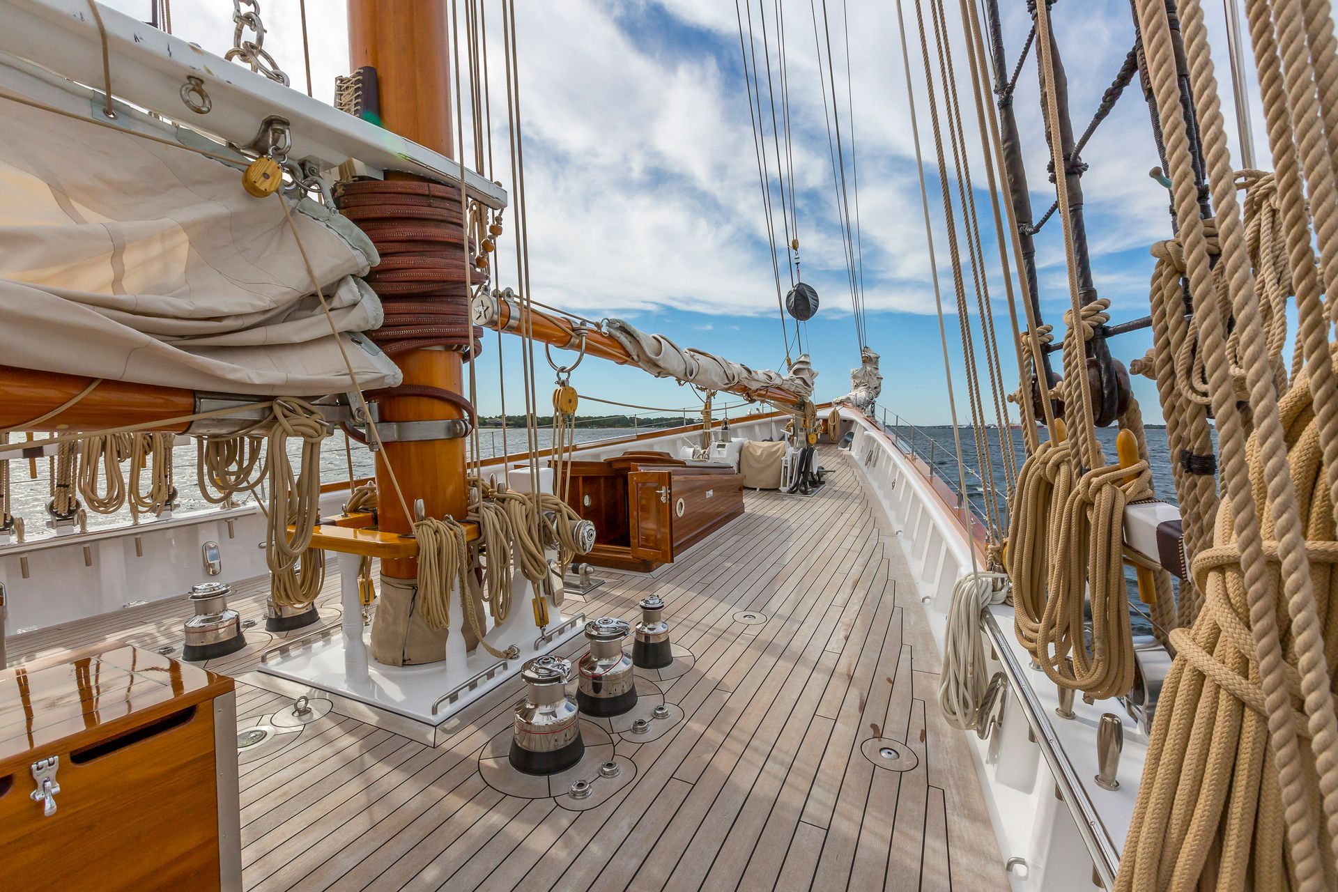 Sailing ship deck with wooden planks, rigging, ropes, and blue sky over the ocean