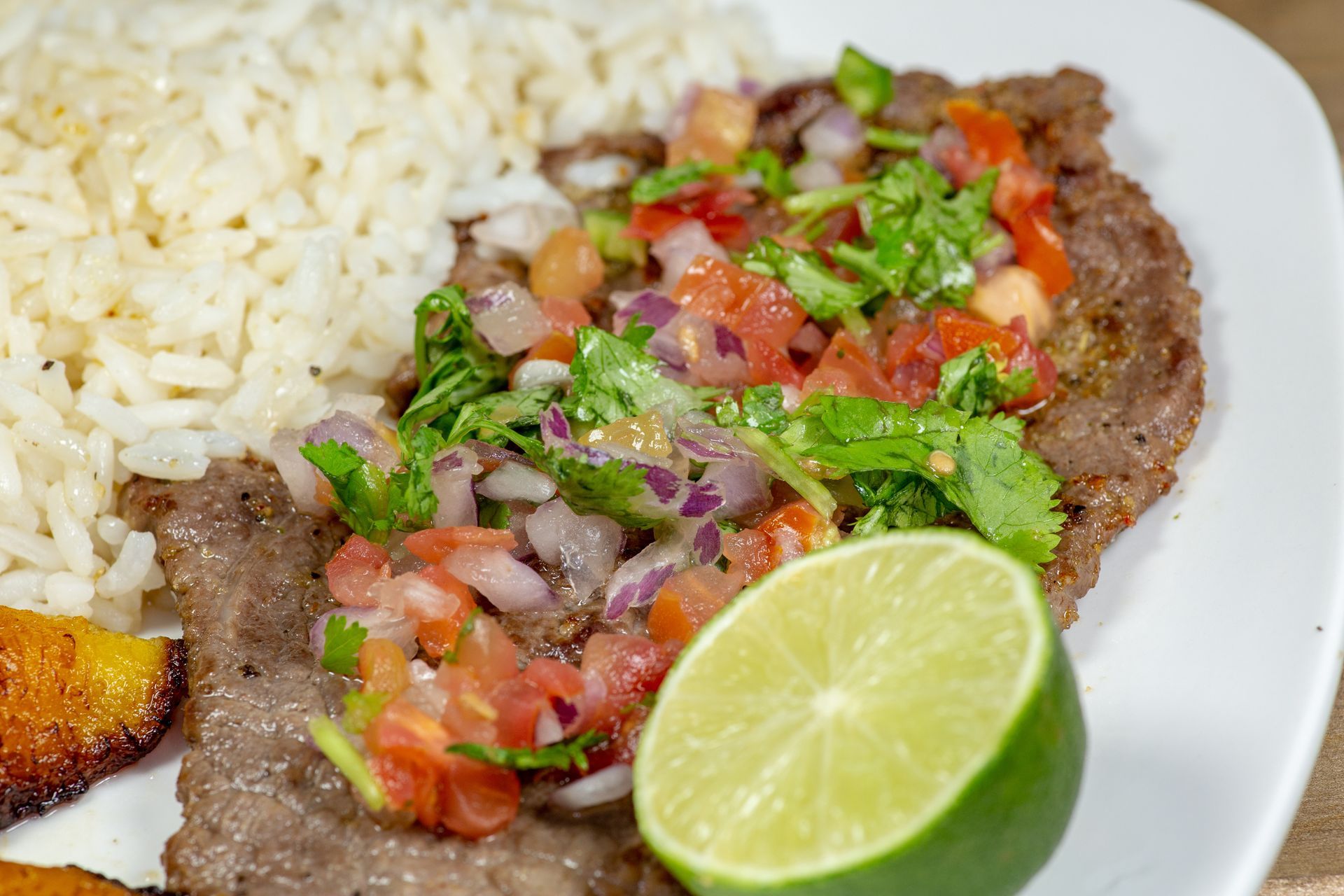 Plate with rice, grilled meat topped with salsa, fried plantain, and a lime wedge