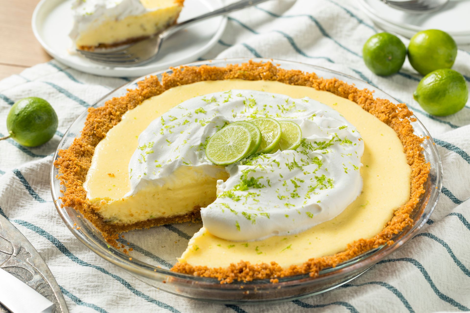 Key lime pie with whipped cream and lime slices on a cooling rack, with a slice removed