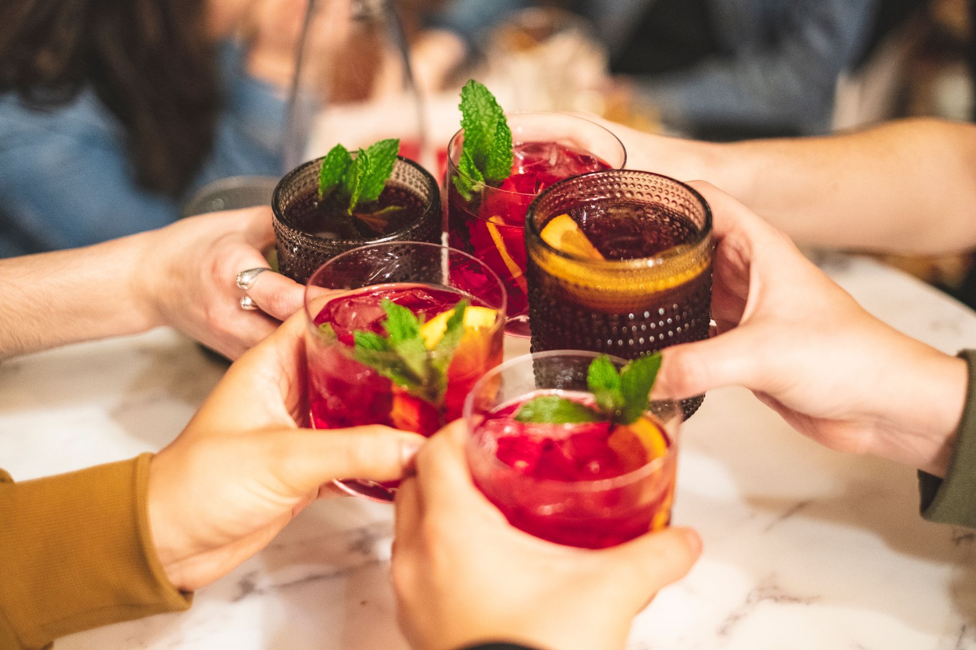 Hands raising colorful cocktails with mint around a table in a social toast