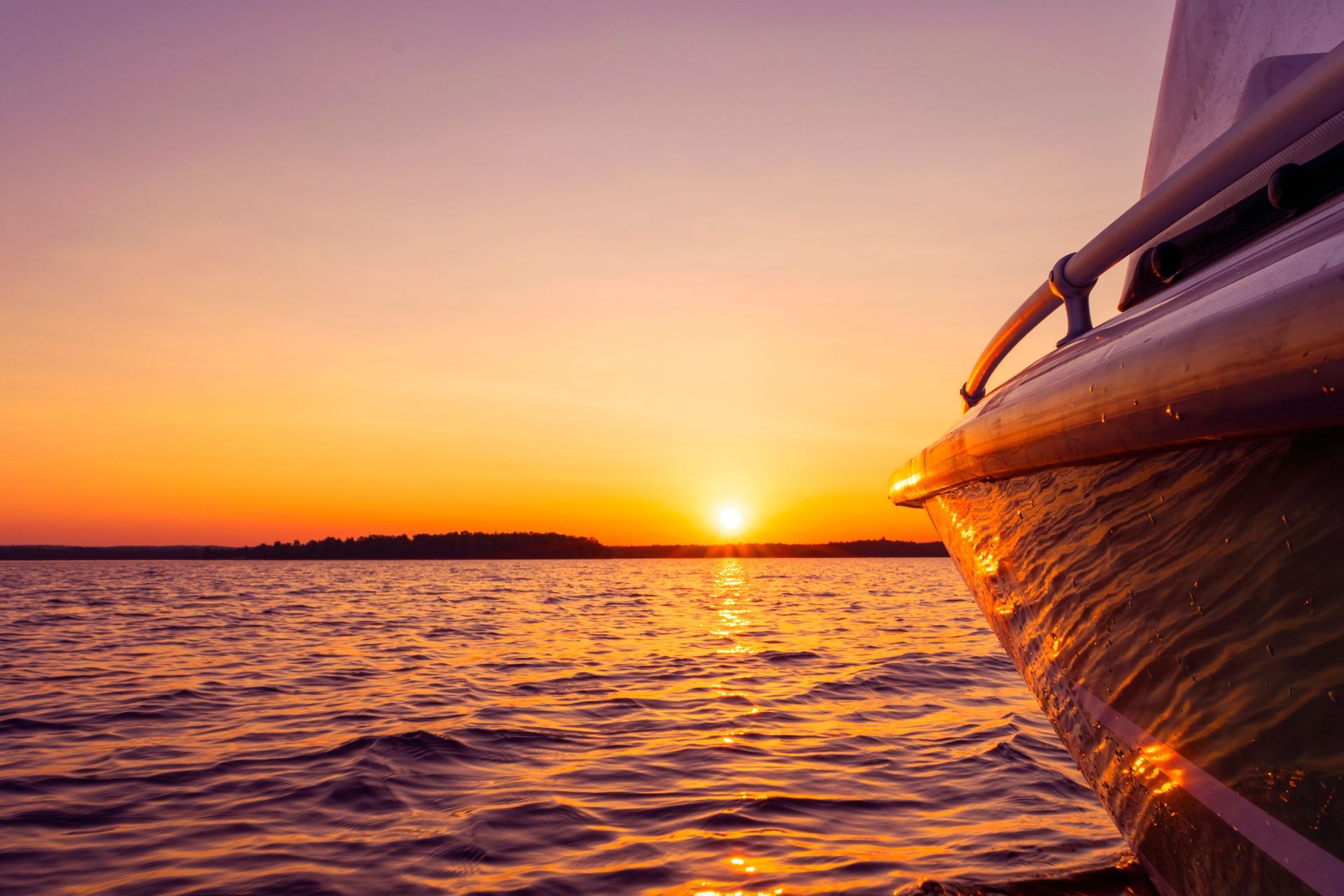 Sunset over calm ocean with a boat’s bow at right and orange reflections on the water