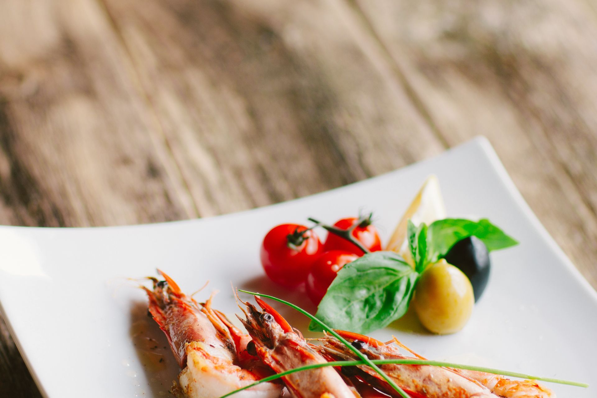 Plated shrimp with cherry tomatoes, basil, and olives on a white dish.
