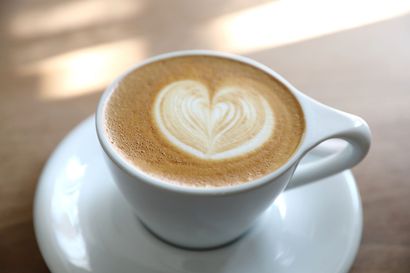 White cup of latte with heart-shaped foam art on a saucer
