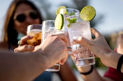 Friends toasting with lime-garnished drinks outdoors in sunlight
