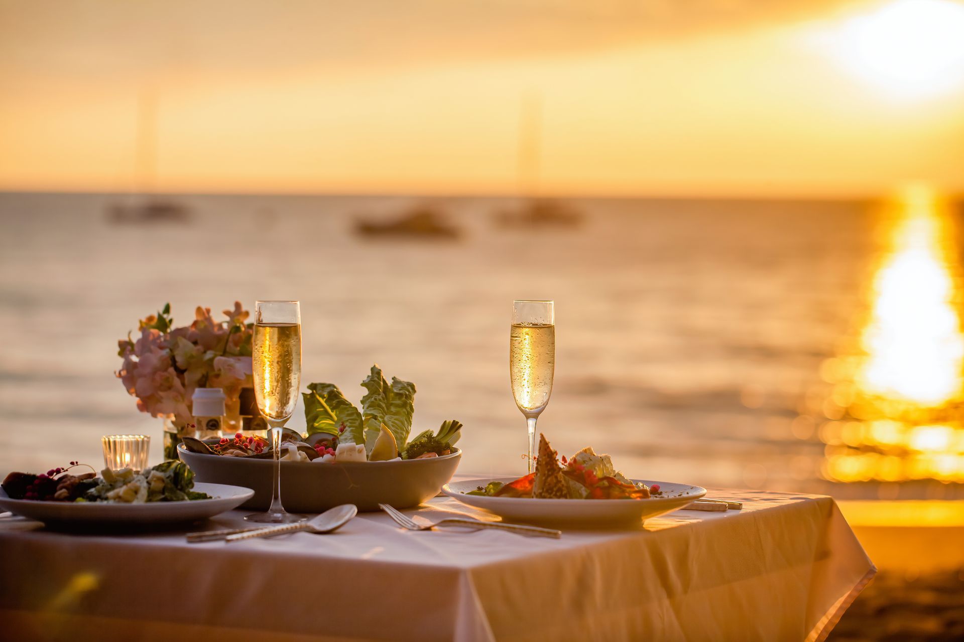 Romantic seaside dinner table set at sunset with champagne and flowers, overlooking the ocean