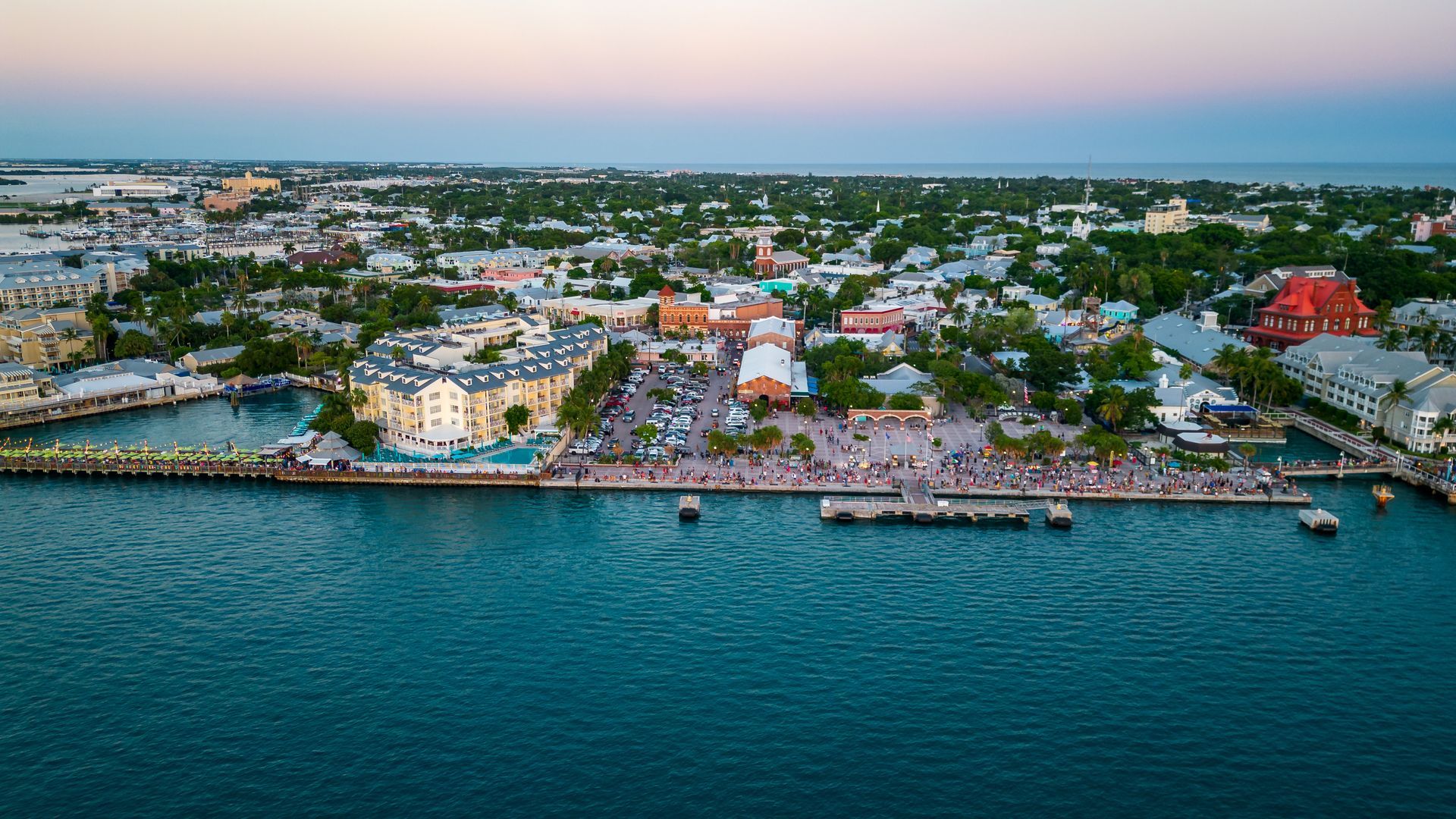 Aerial view of a colorful seaside town with waterfront buildings, docks, and calm blue water at sunset