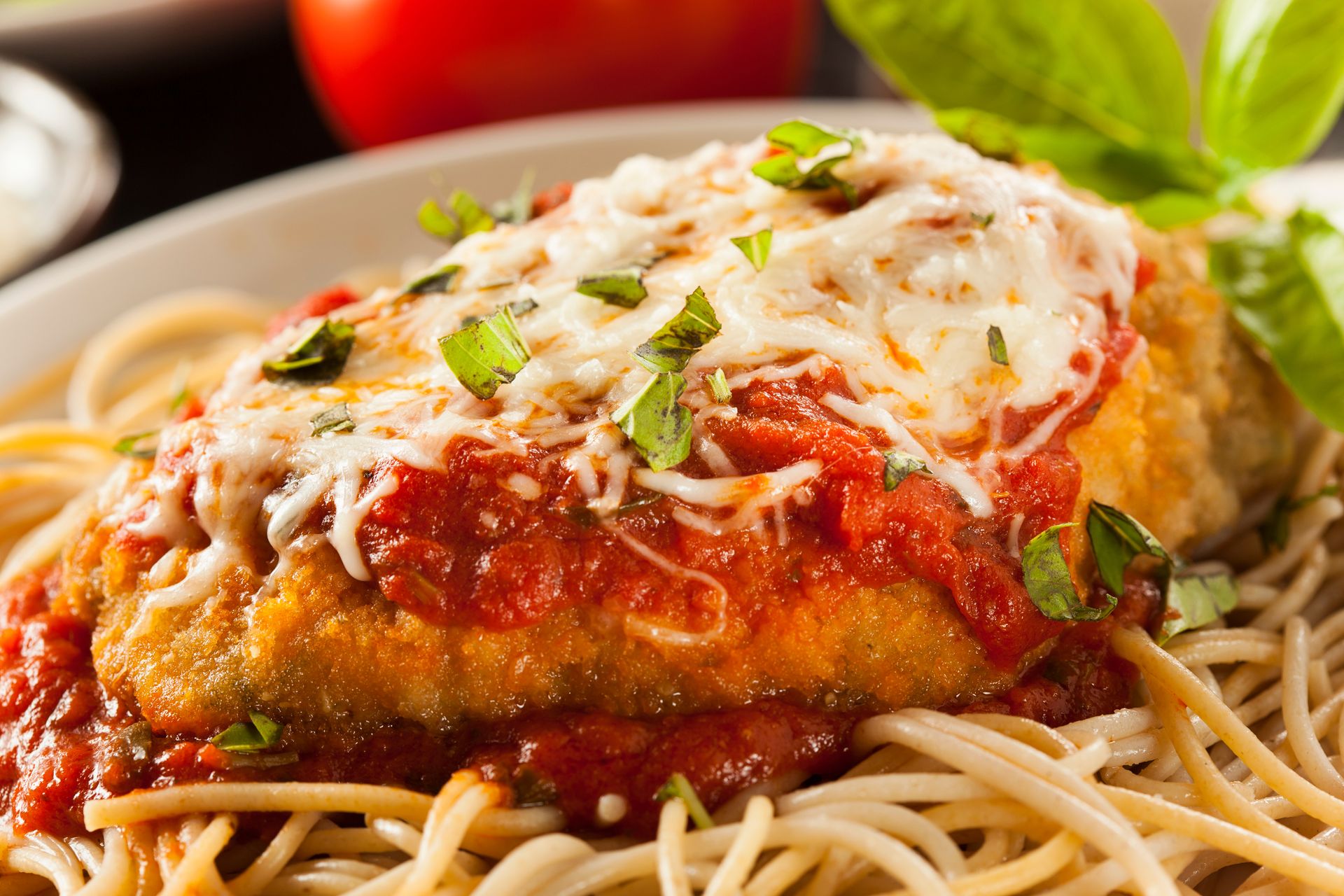 Spaghetti topped with marinara, melted cheese, and basil on a white plate
