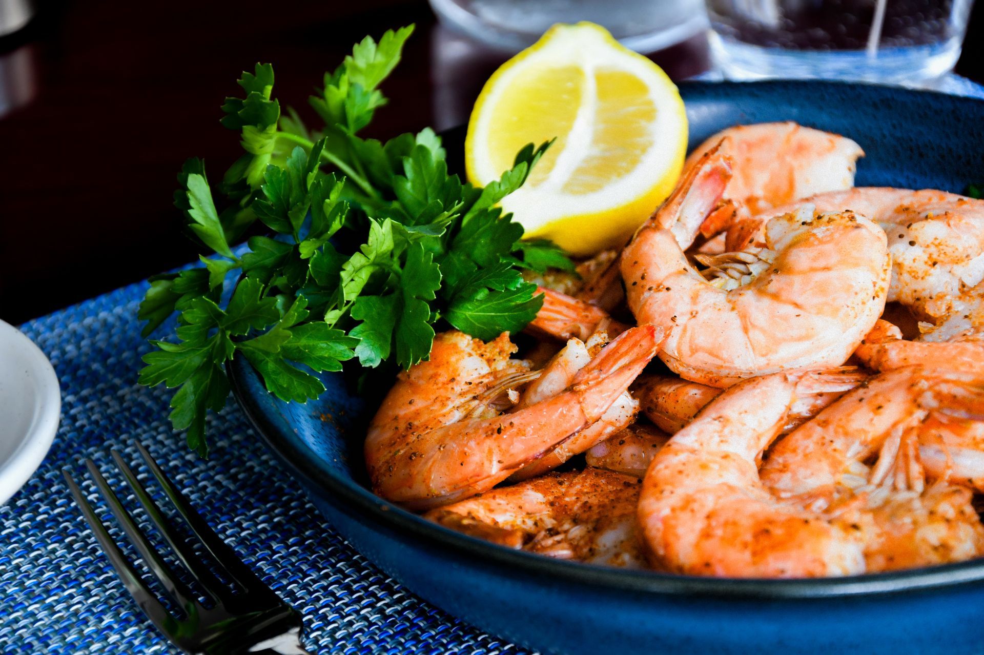 Plated shrimp with parsley and a lemon wedge on a dark table