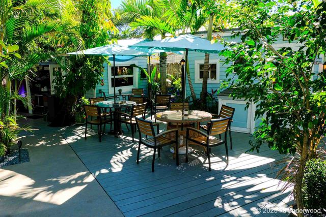 Outdoor patio with tables, chairs, and umbrellas amid lush greenery around a small house