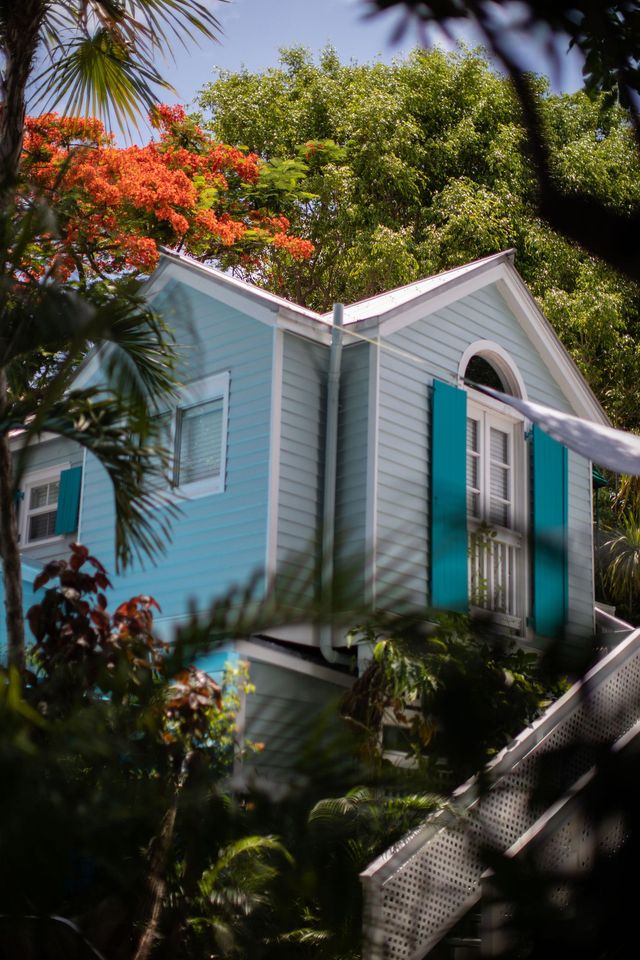 Pastel blue house with white trim and teal shutters nestled among lush tropical greenery