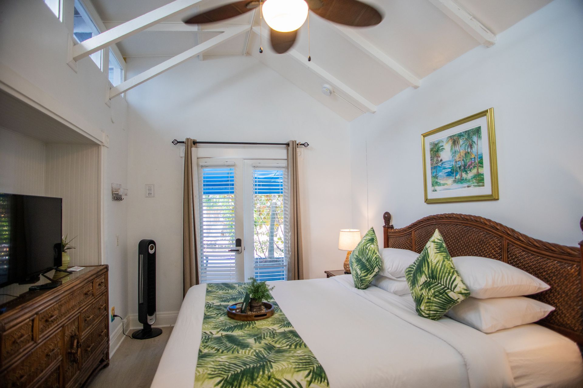 Bright bedroom with white vaulted ceiling, wicker bed, French doors, and tropical decor