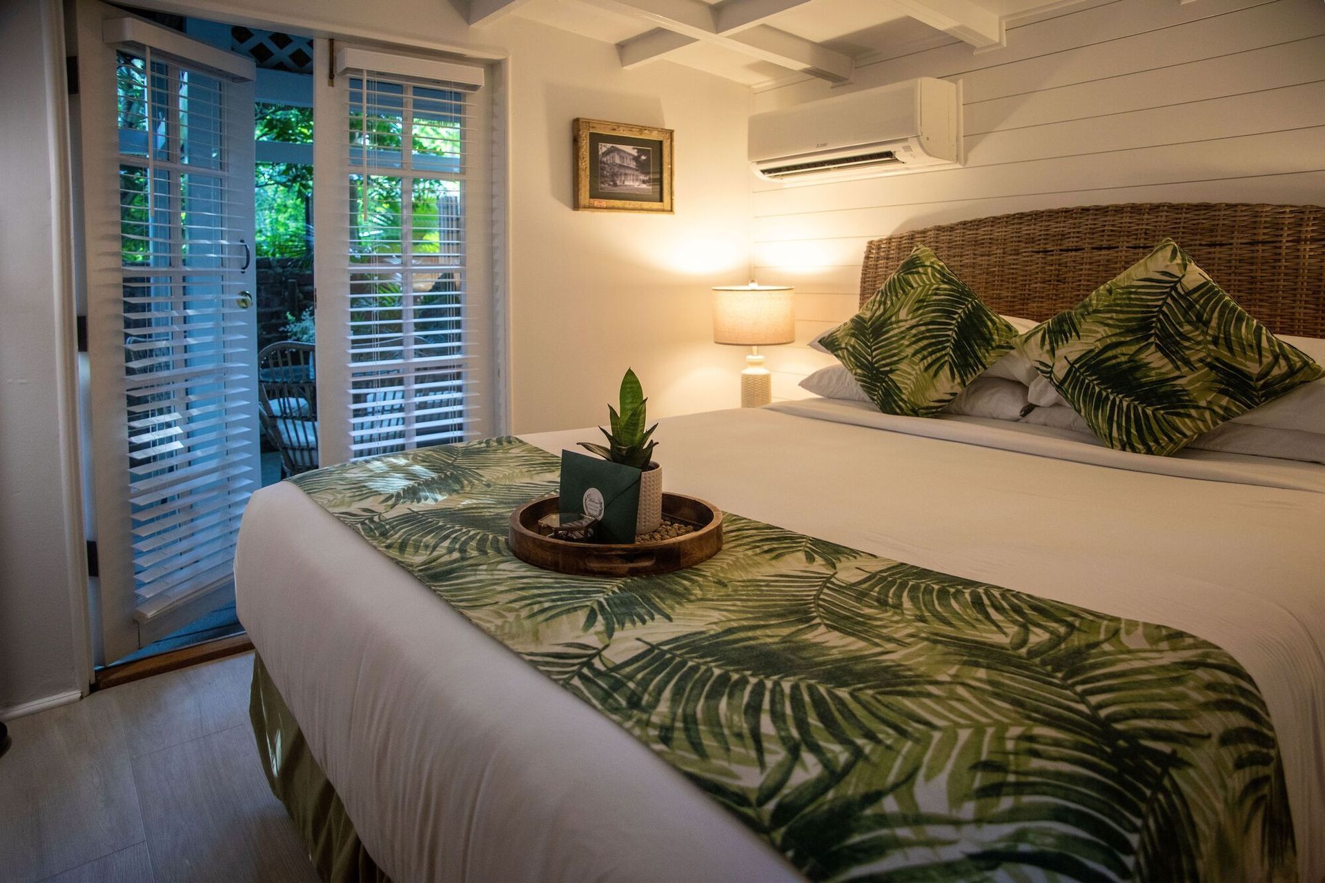 Cozy bedroom with a bed, tropical leaf bedding, bedside lamp, and French doors to a balcony