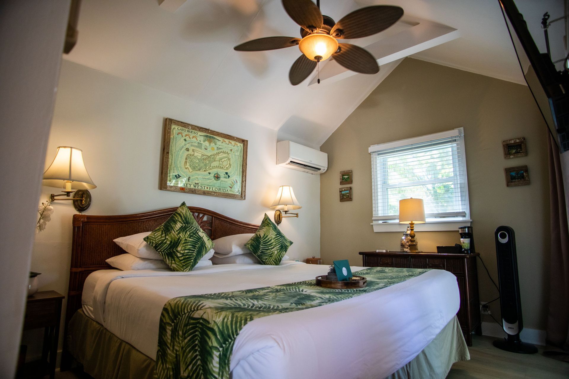 Cozy bedroom with a king bed, ceiling fan, lamps, green accents, and natural light from a window.