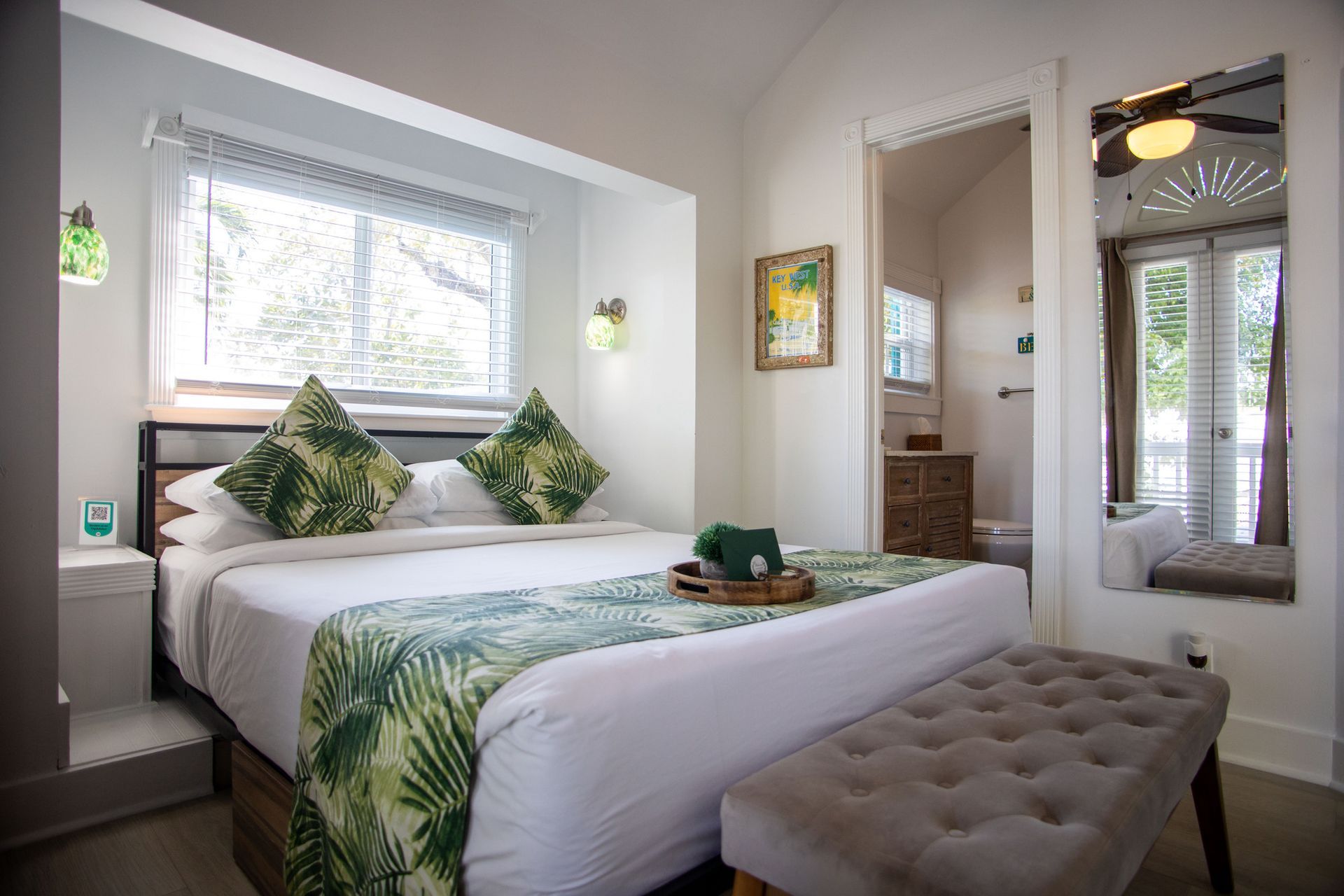 Bright bedroom with a neatly made bed, green accents, and a tufted bench by a large window.