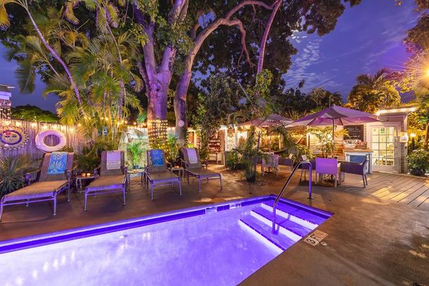 Illuminated outdoor pool patio with lounge chairs, trees, and warm evening lighting