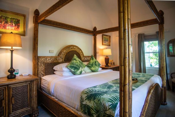 Warm tropical bedroom with four-poster bed, green pillows, wooden furniture, and balcony view