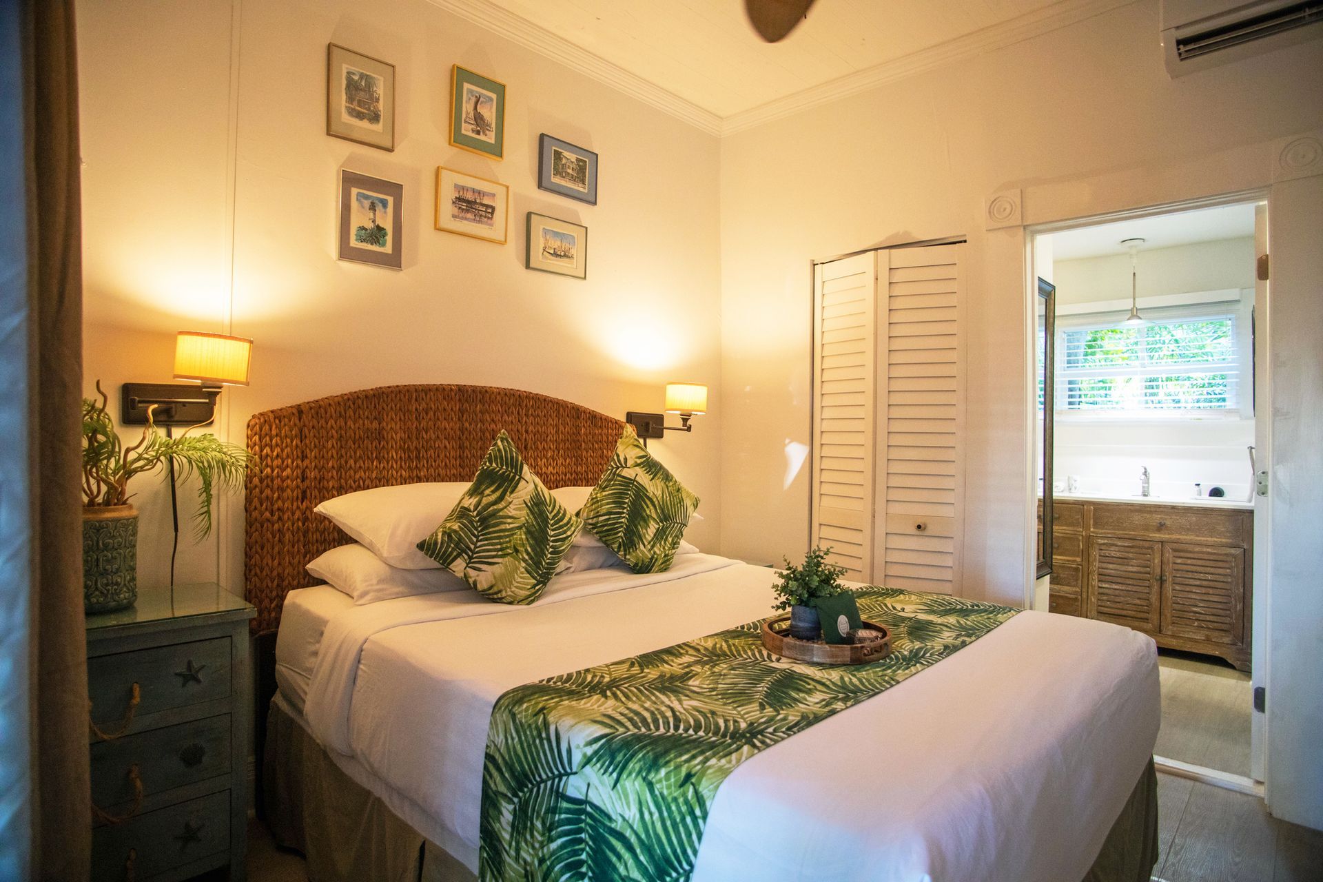 Cozy bedroom with a bed, green accents, wall art, lamps, and an open door to a bright bathroom.