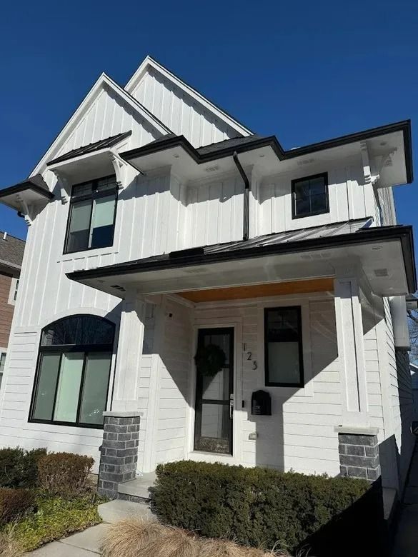 White two-story house with dark trim, front porch, and peaked roof under a clear blue sky